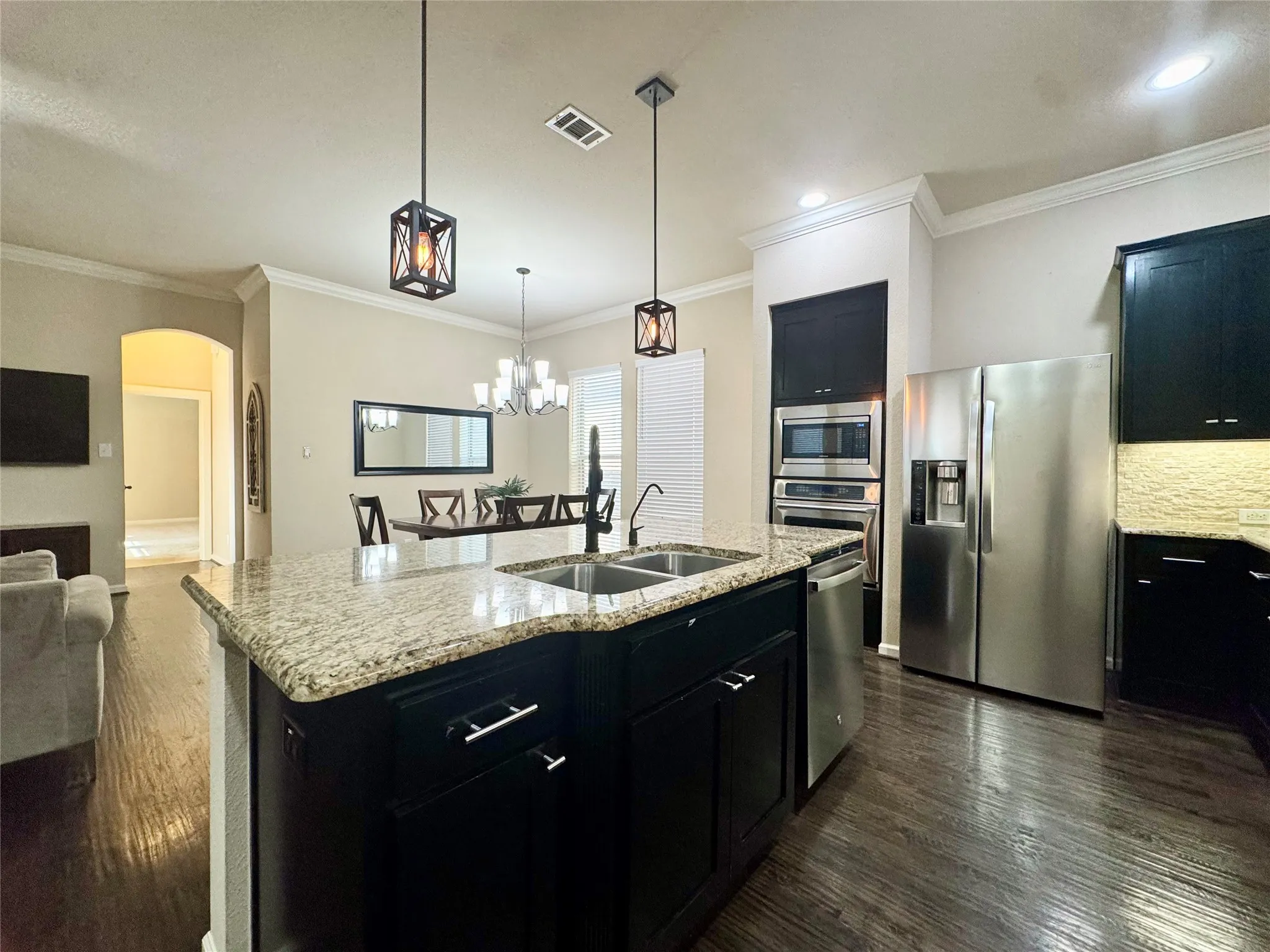 Kitchen featuring a central island with a granite countertop, stainless steel appliances, dark wood-finish flooring, recessed lighting, and crown molding