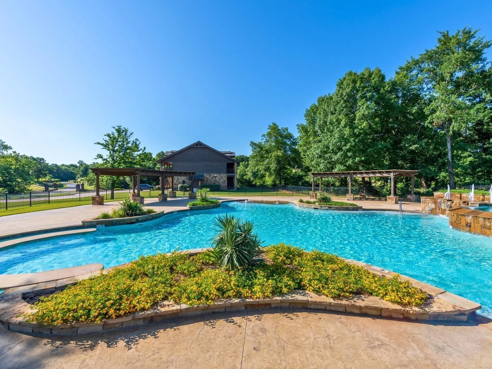Expansive outdoor pool with a river feature, adjacent pergolas, and a stone water feature, surrounded by mature trees
