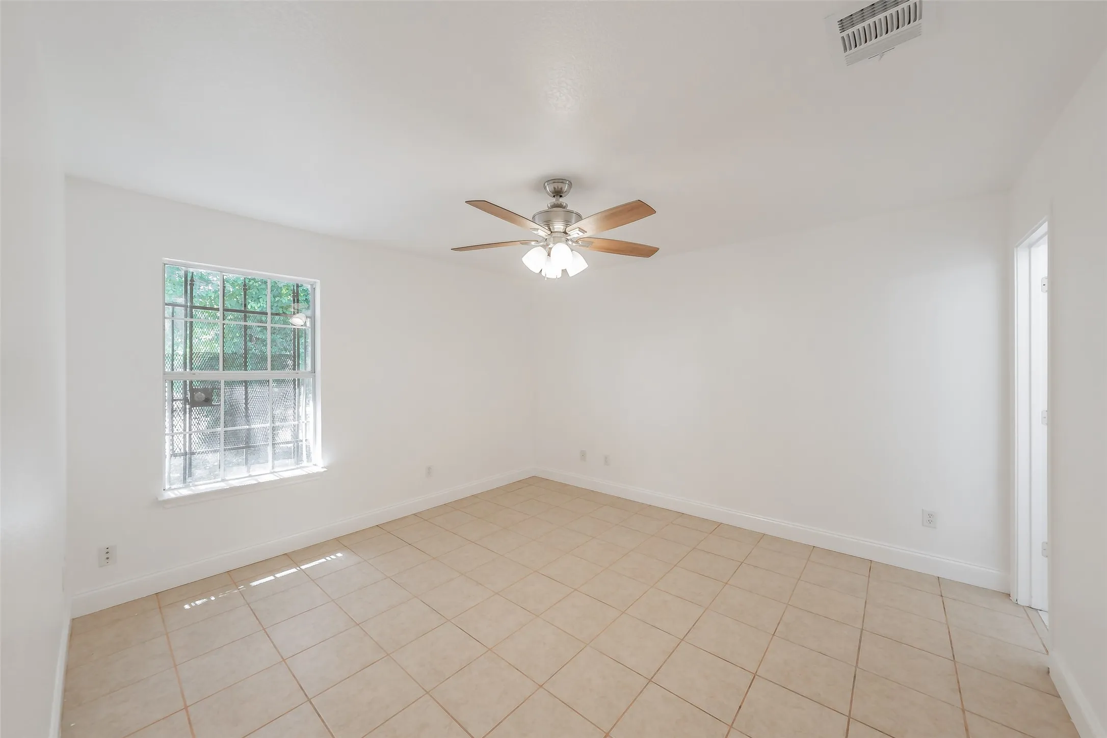 Tile flooring, ceiling fan with light fixture, window with security bars, white walls, white trim