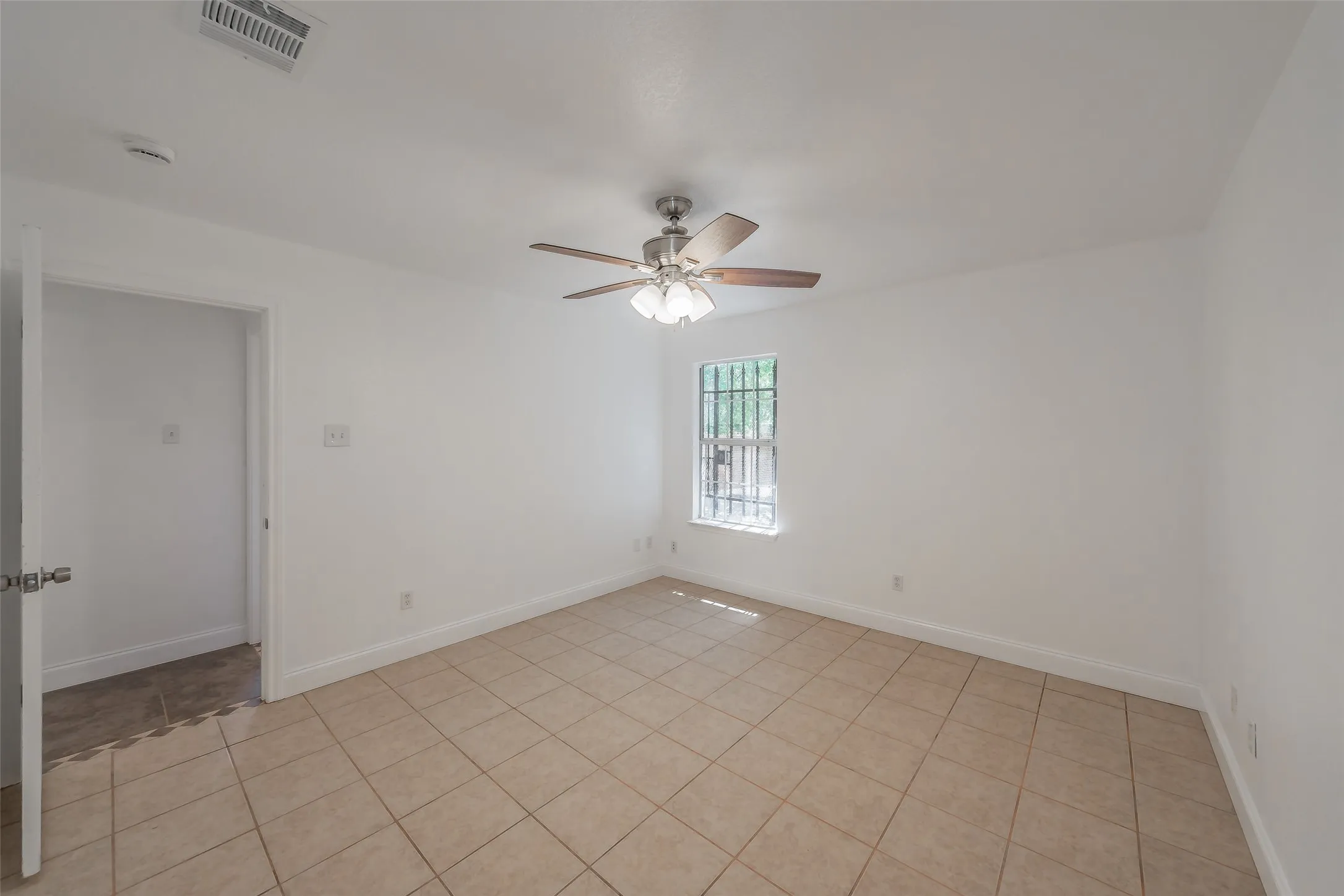 Room featuring tile flooring, white walls, a ceiling fan with light fixture, and a window