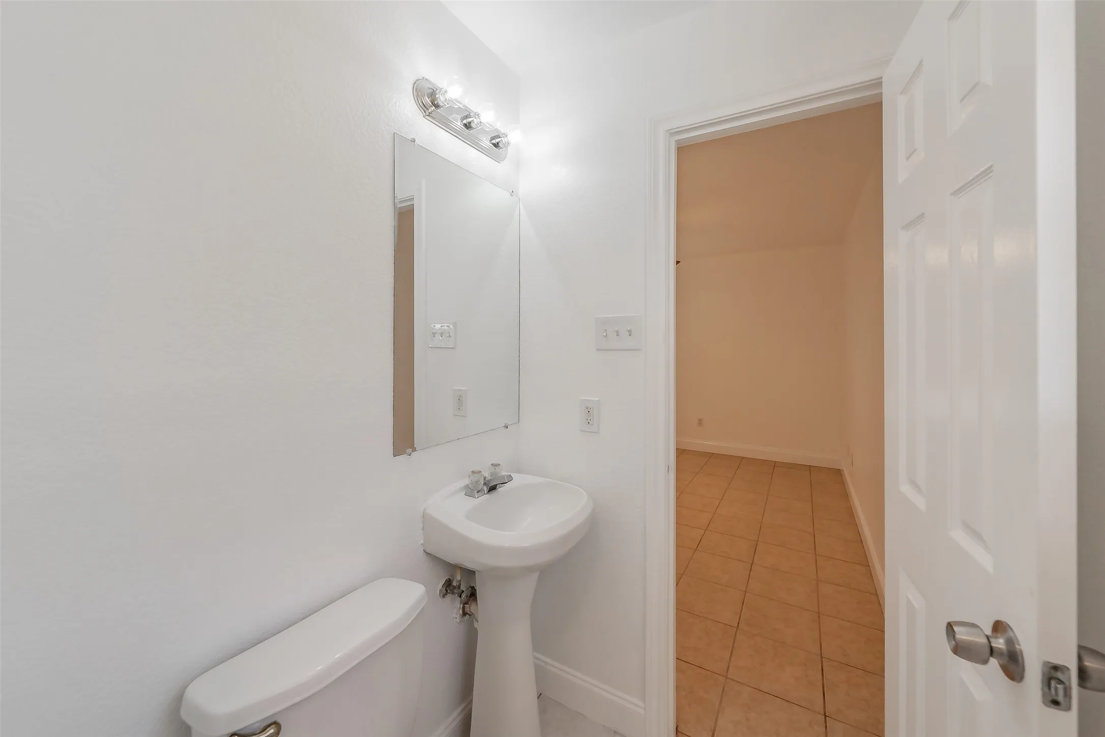 White pedestal sink with a wall-mounted mirror, overhead vanity lighting, and a white toilet