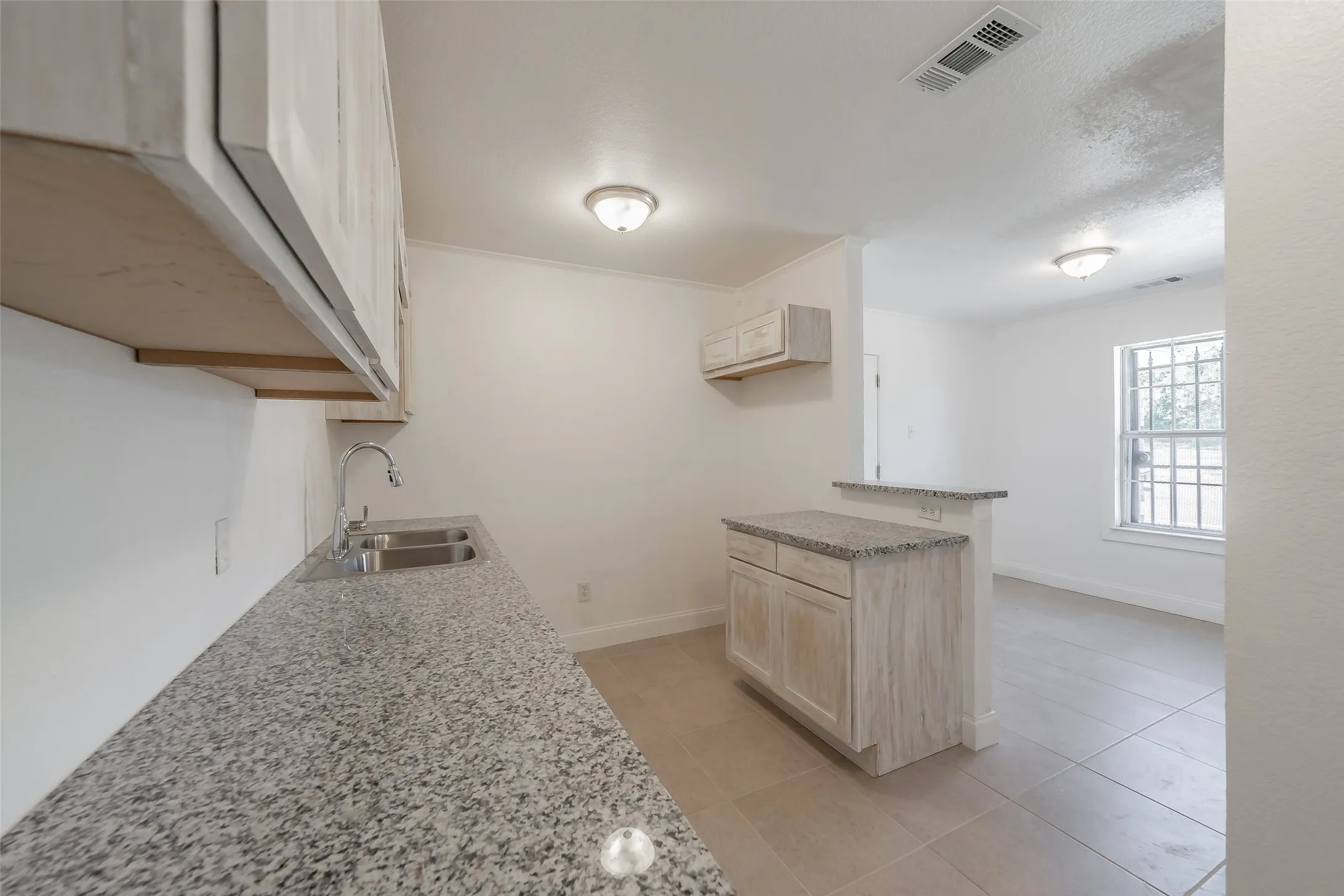 Kitchenette featuring light-toned cabinetry, a stainless steel double sink, speckled countertops, and an integrated breakfast bar