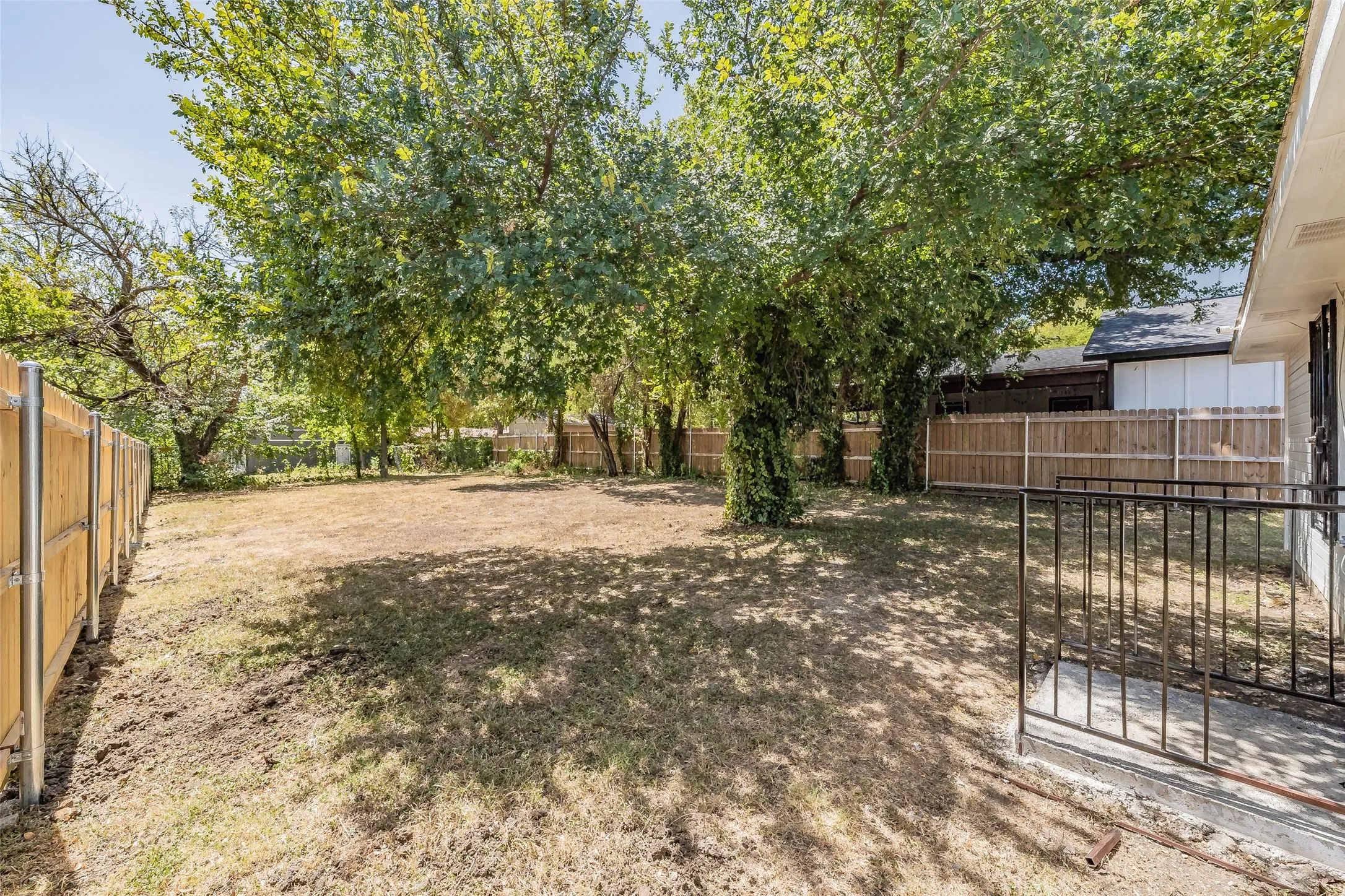 Expansive rear yard featuring mature trees, a wood privacy fence, and a concrete patio with a black metal railing