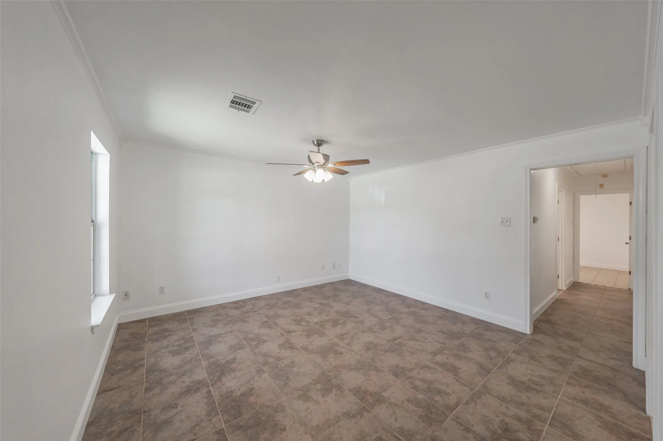 Spacious room featuring tile flooring, a window providing natural light, a ceiling fan, and crown molding