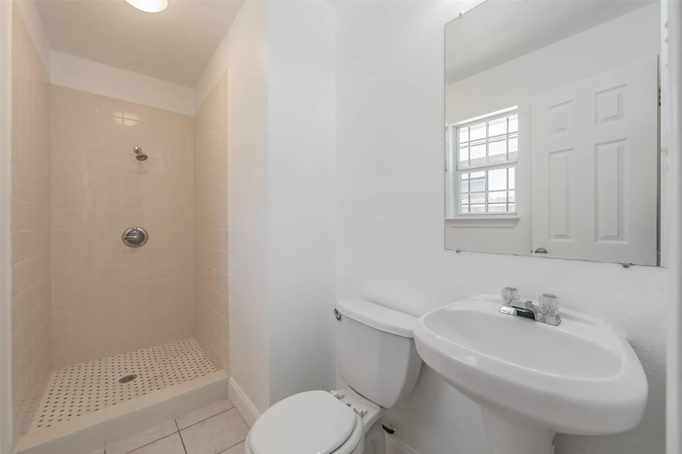 White pedestal sink with a chrome-finish faucet and a tiled shower with a chrome-finish shower head