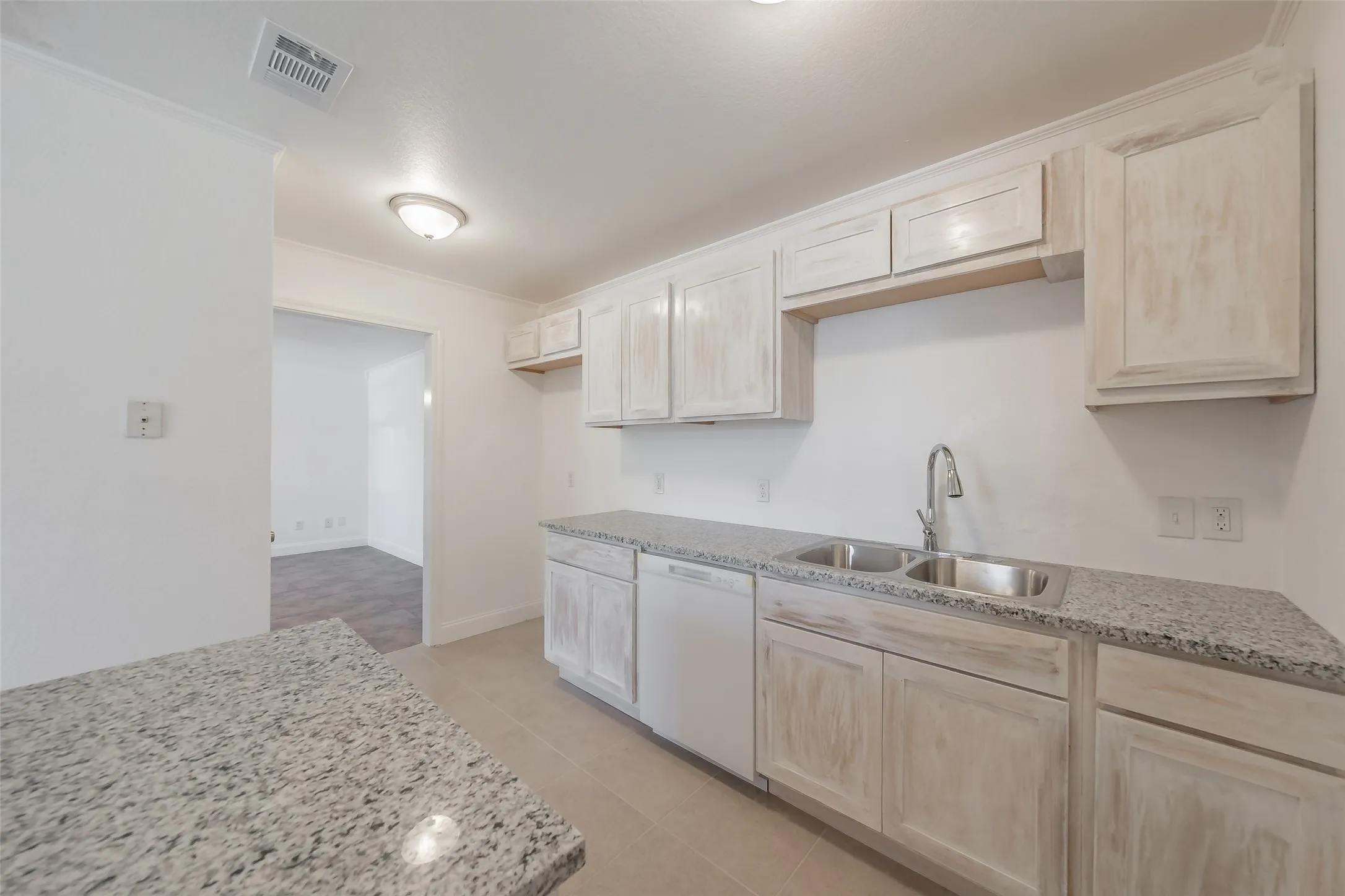 Kitchen featuring granite-style countertops, dual stainless steel sinks, a gooseneck faucet, and light wood-finish cabinetry
