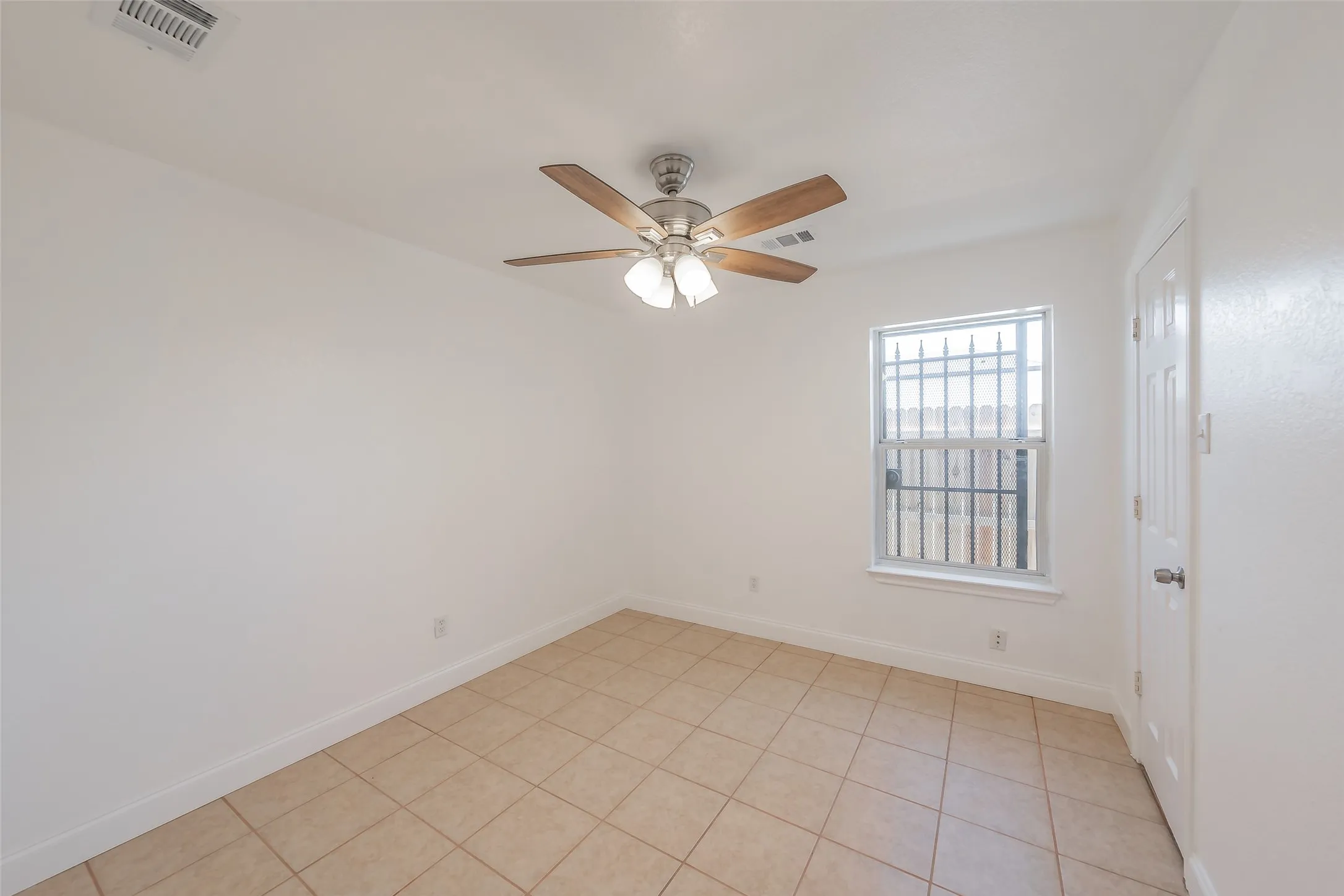 Tile flooring, ceiling fan with light fixture, window with security bars, white interior door