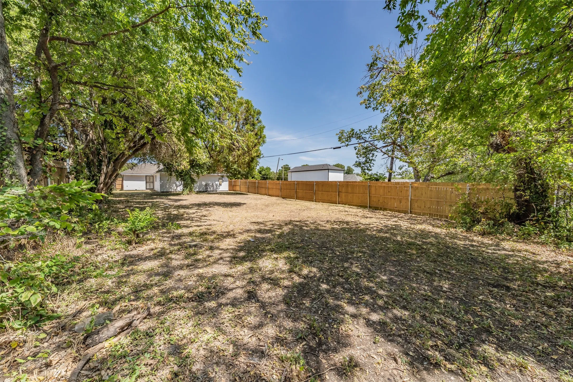 Expansive outdoor space featuring a wood fence, mature trees, and a clear, level lot