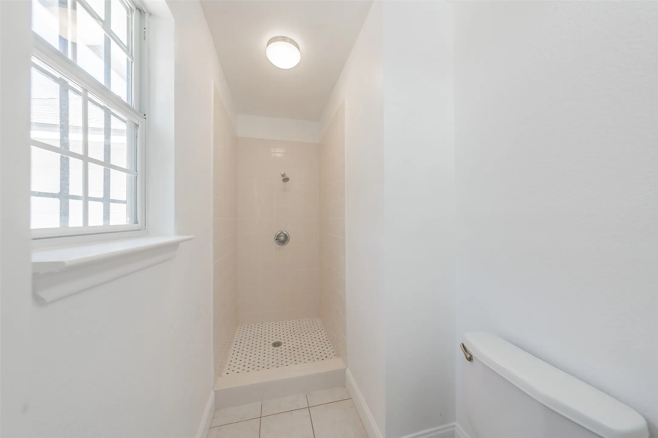Recessed shower with light-toned wall tile, chrome shower fixtures, and a white tiled floor