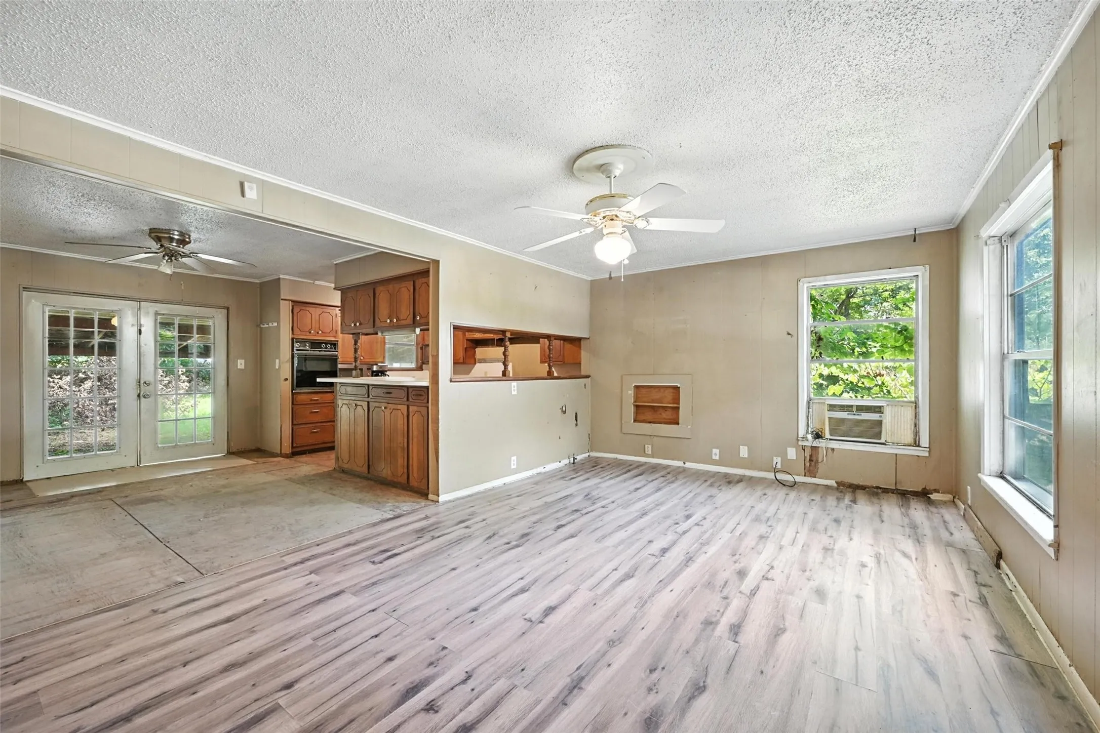 Unfurnished living room with a ceiling fan, healthy amount of natural light, light wood-style floors, a textured ceiling, and french doors