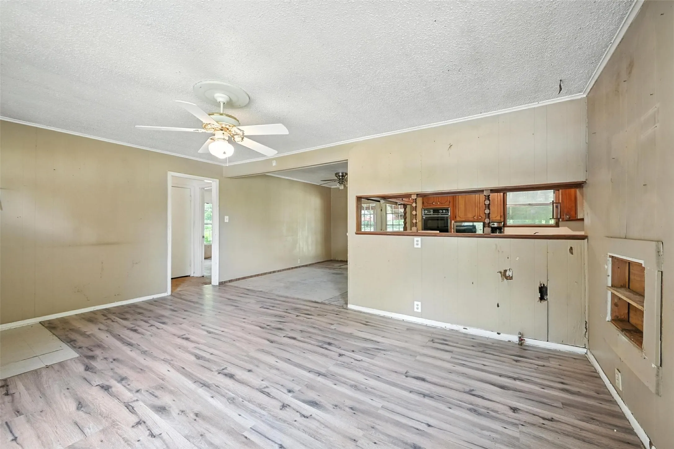 Unfurnished living room featuring a textured ceiling, light wood-style floors, plenty of natural light, a ceiling fan, and crown molding