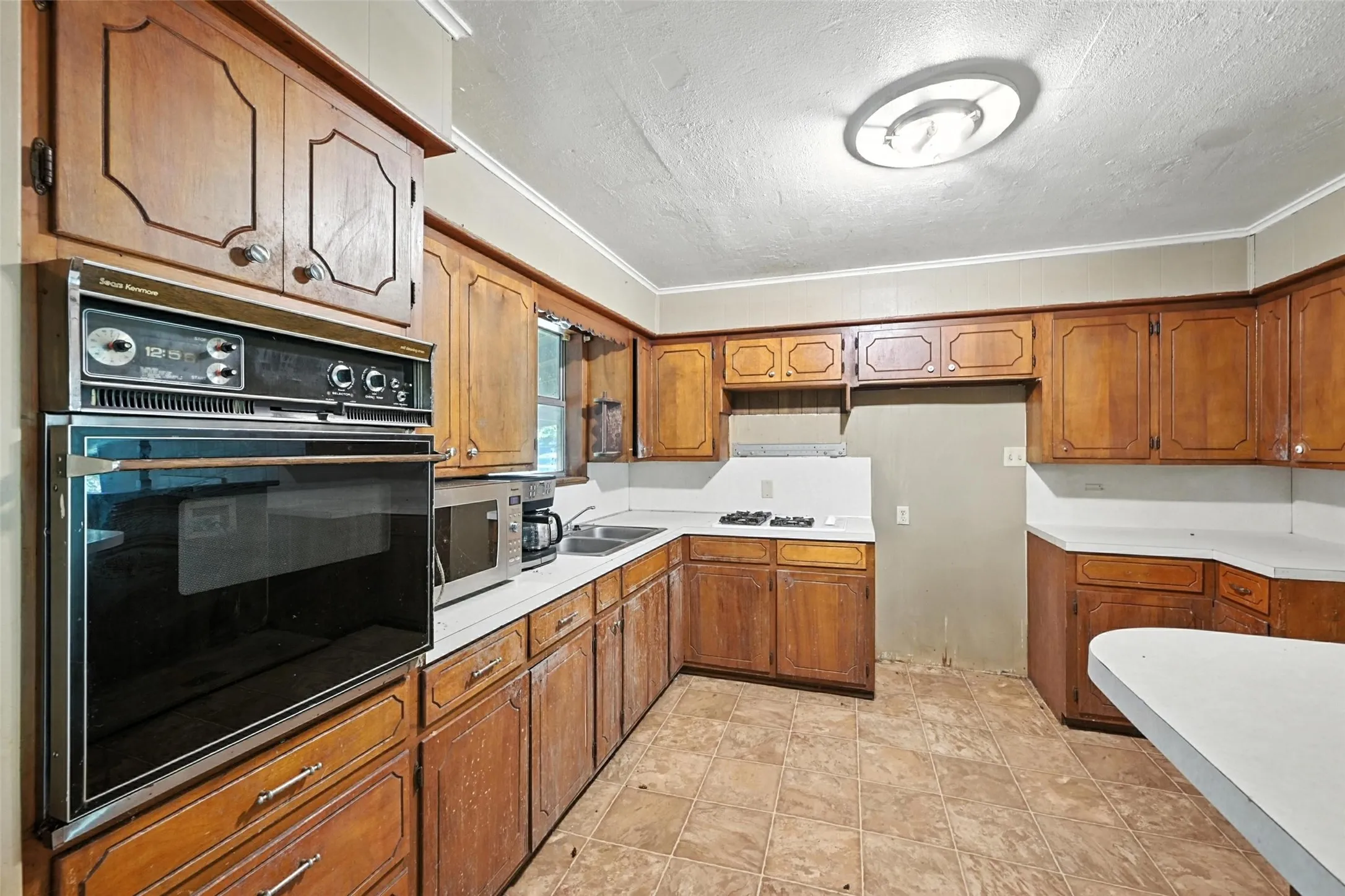 Kitchen featuring oven, wood finish cabinets, light countertops, a textured ceiling, and stainless steel microwave