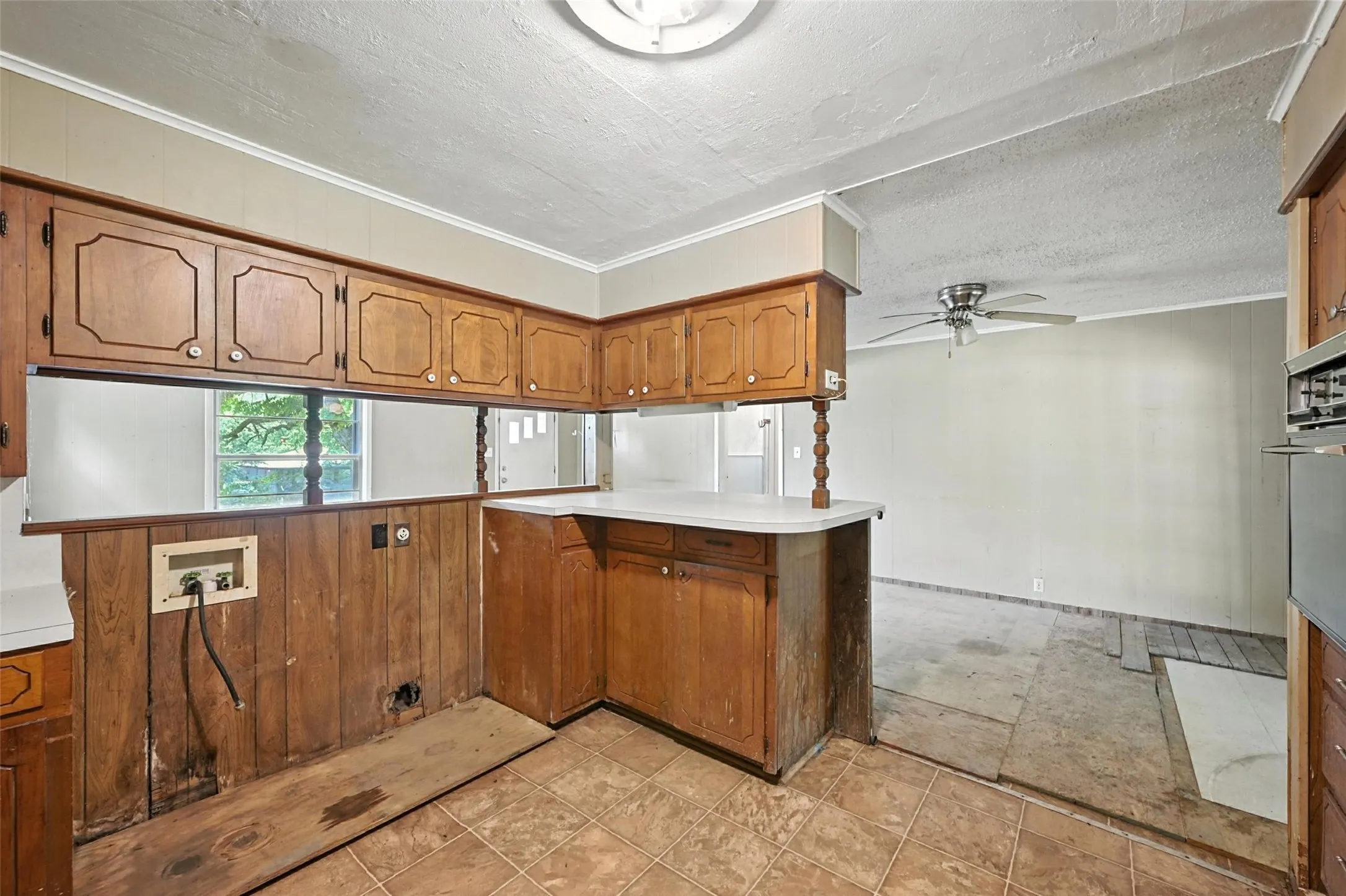Kitchen with wood finish cabinets, light countertops, a peninsula, wooden walls, and a ceiling fan
