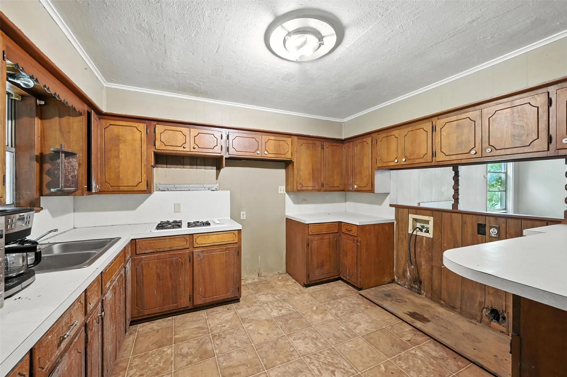 Kitchen featuring light countertops, wood finish cabinetry, a textured ceiling, crown molding, and white gas cooktop