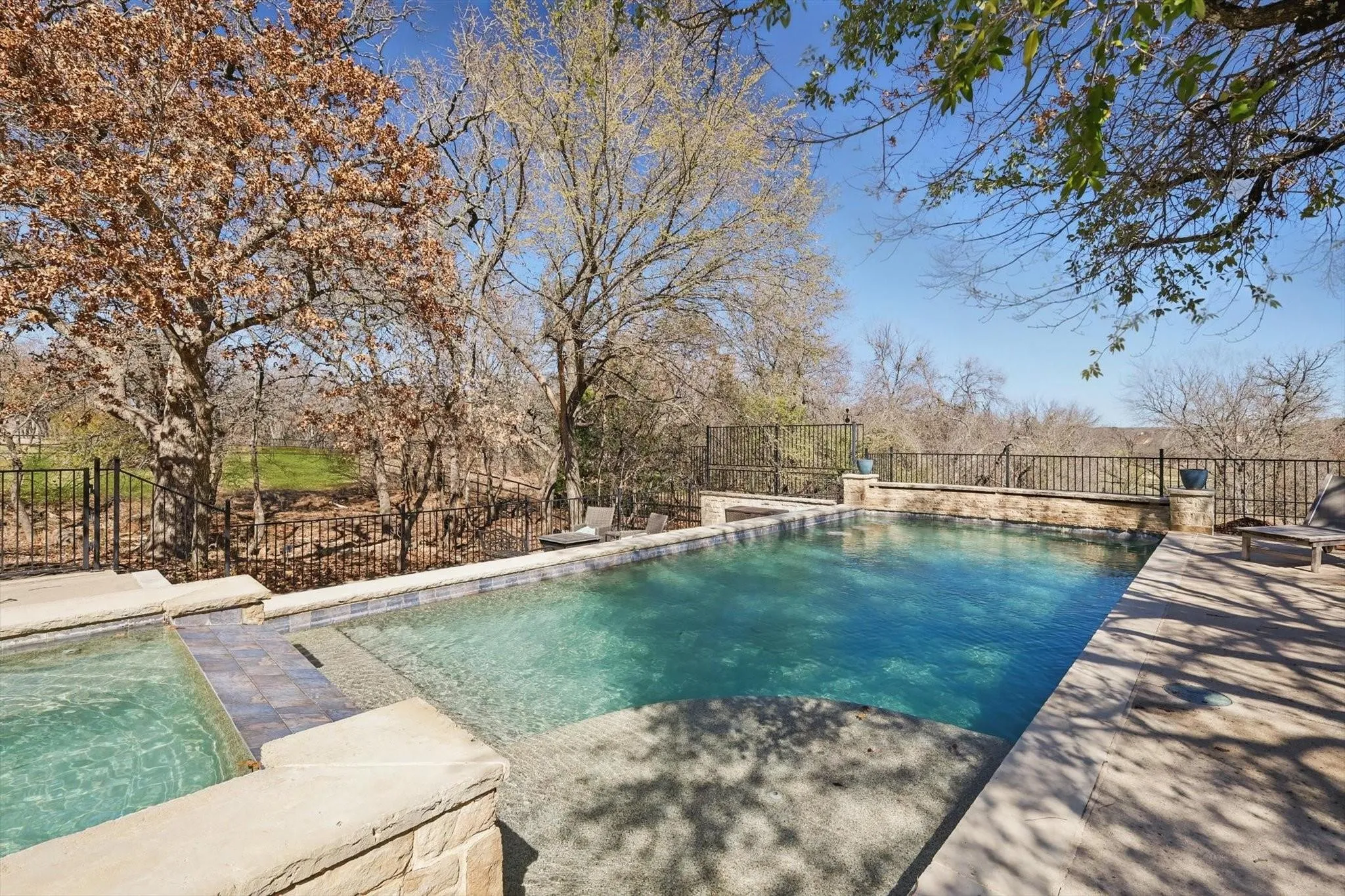 Swimming pool with stair entry, patio space, and connected hot tub.