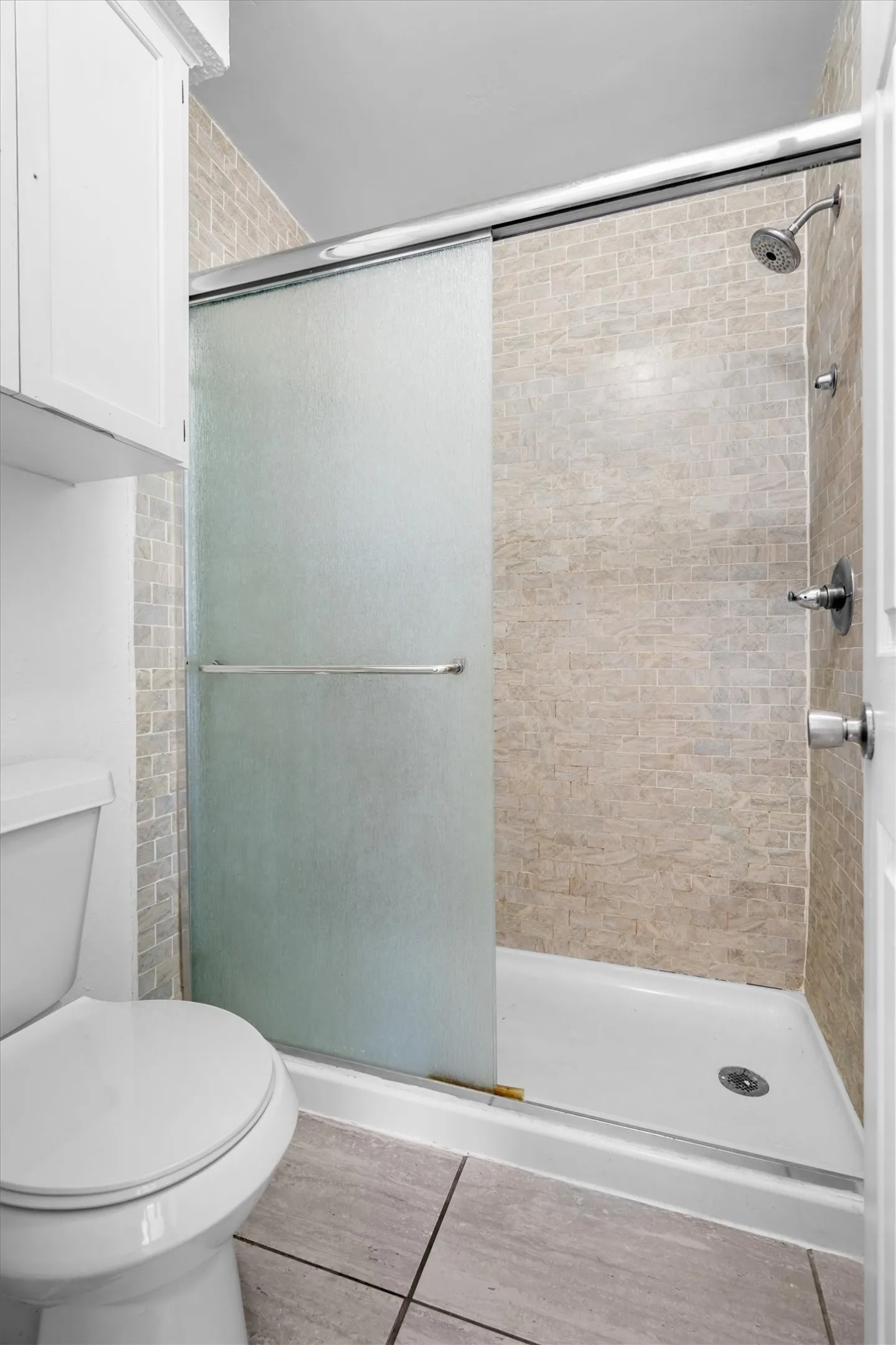 Shower with sliding frosted glass doors, tiled surround, white shower pan, and silver-finish fixtures
