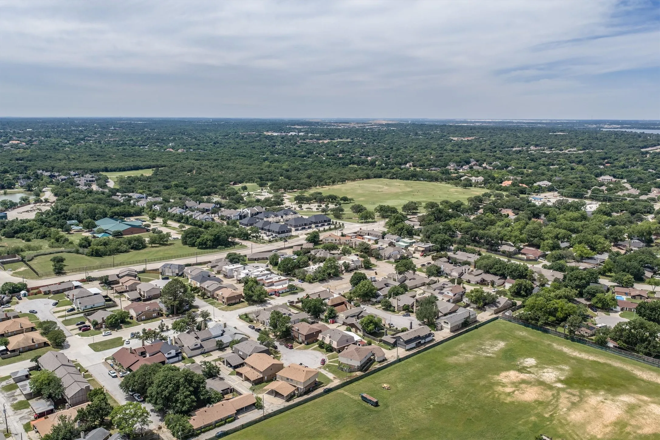 Extensive green spaces and mature trees surround residential properties, with a large sports field visible in the foreground