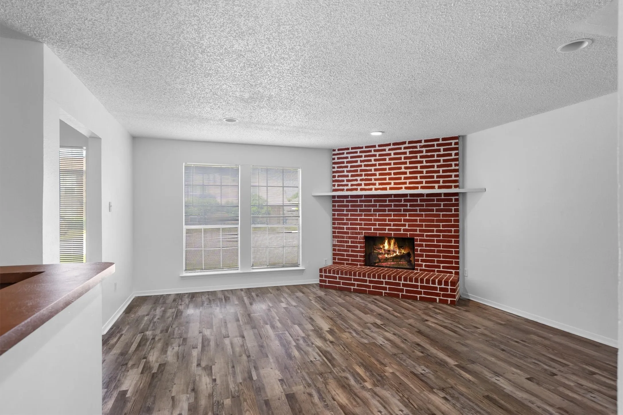 Wood-finish flooring with a corner brick fireplace, white mantel, and multiple windows