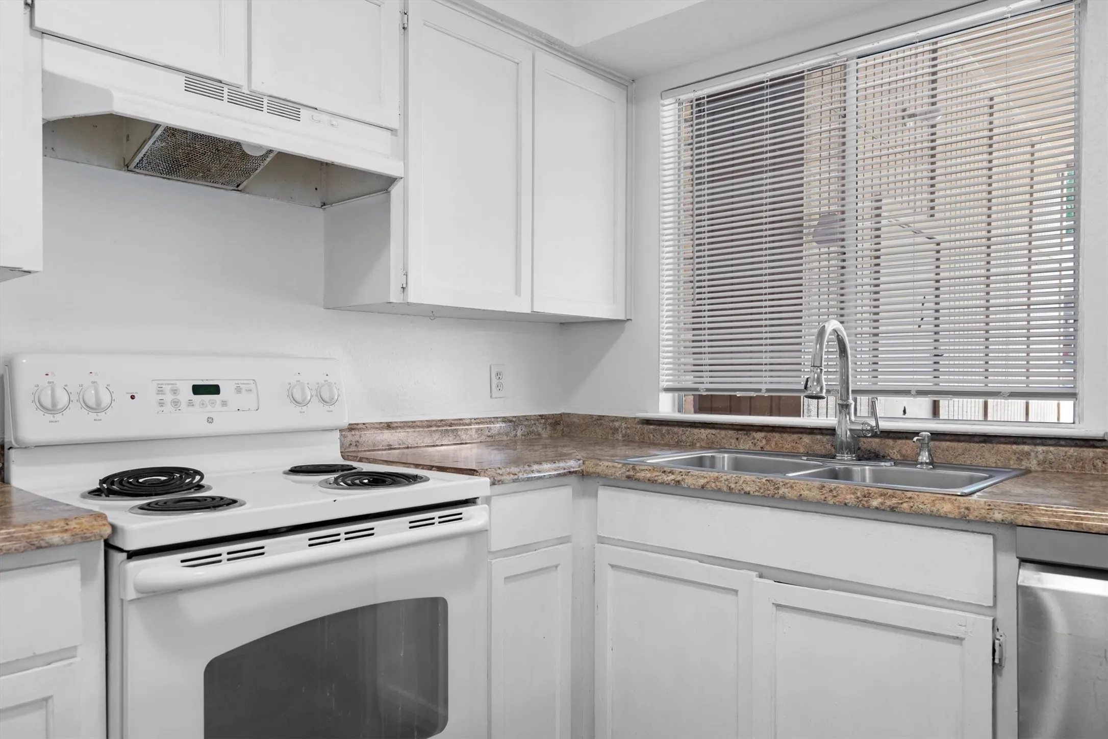 White cabinetry, dual-basin stainless steel sink, pull-down faucet, and a window with horizontal blinds