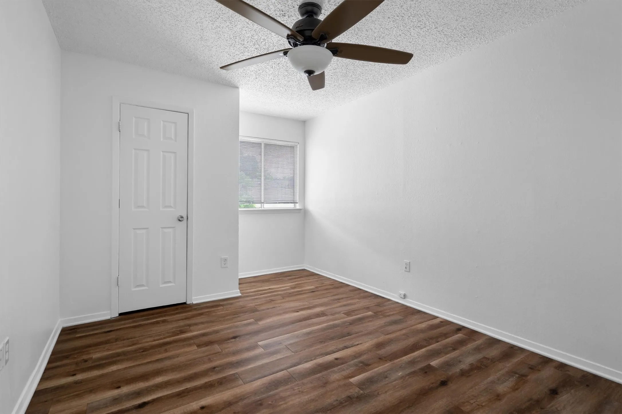 Wood-finish flooring, white walls, and a ceiling fan with integrated lighting