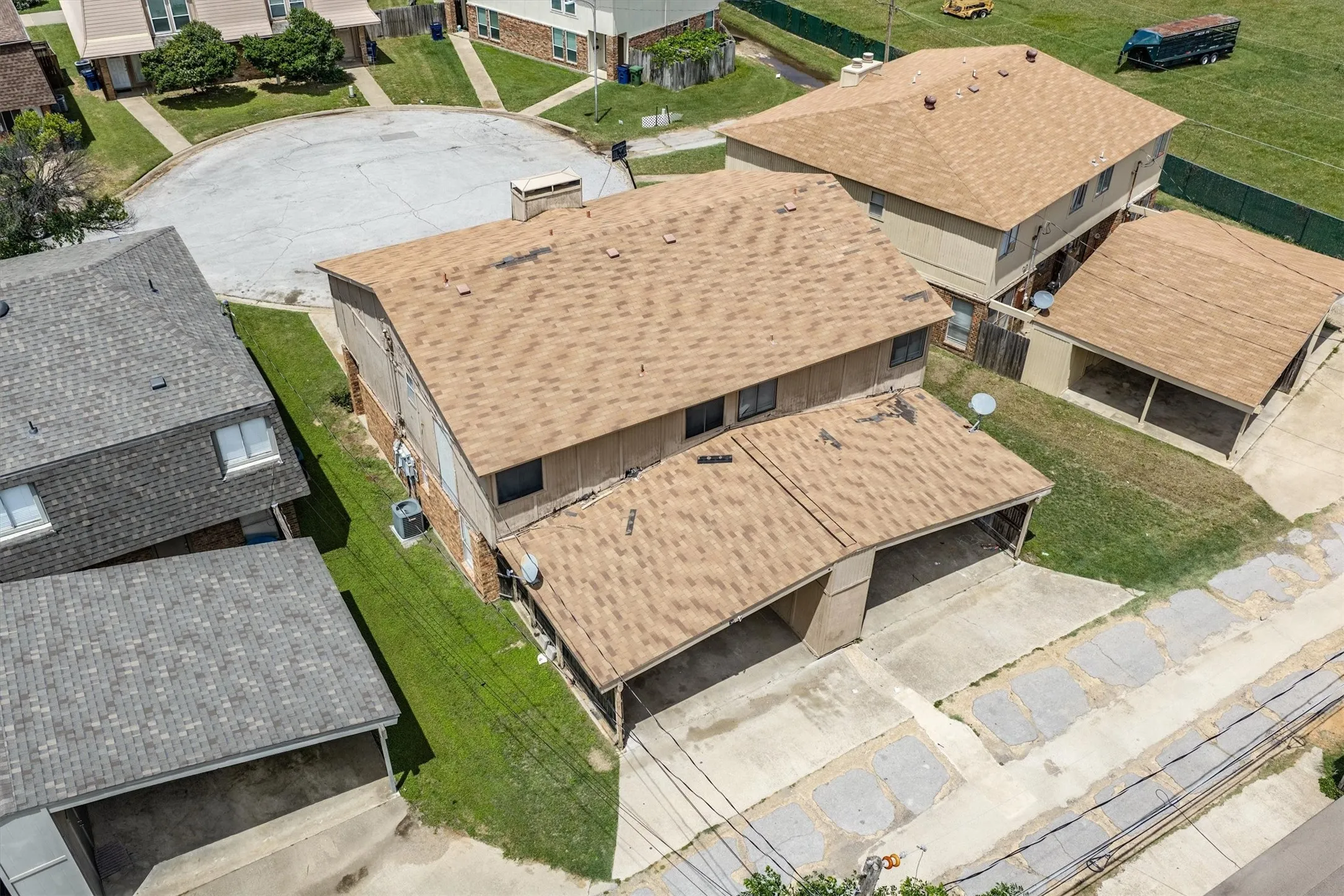 Two-story residential structure with a brown shingle roof, accompanied by an attached carport and a detached carport