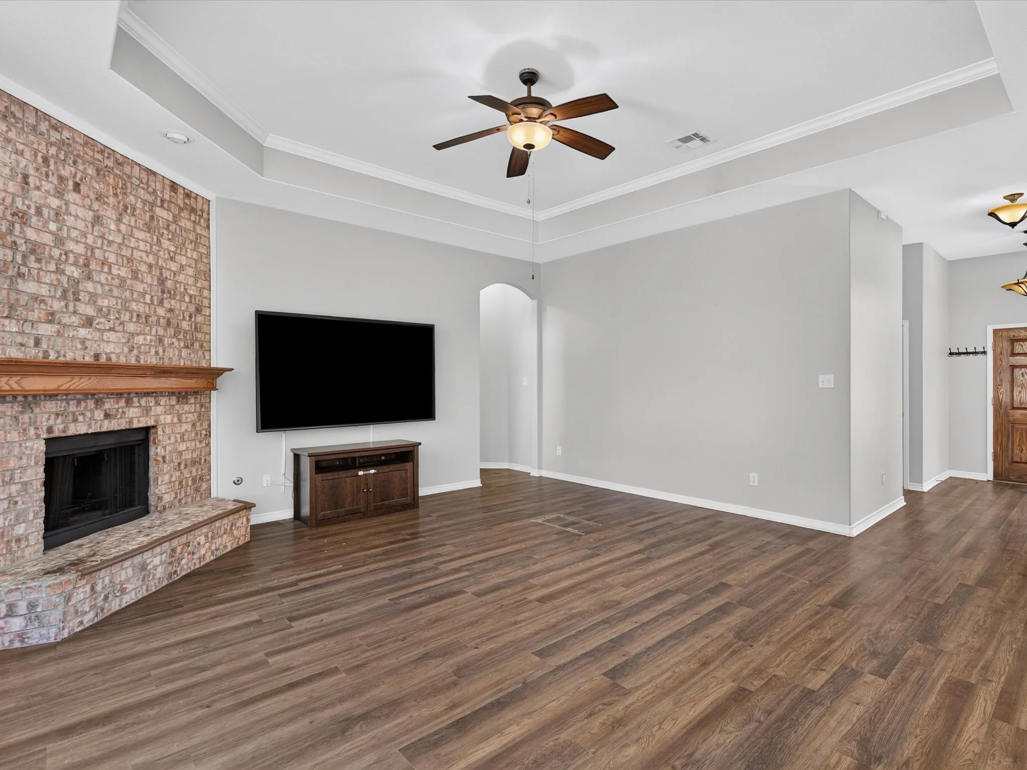 Spacious living room featuring a coffered ceiling with ceiling fan, wood-finish flooring throughout, and a brick fireplace with integrated television mount