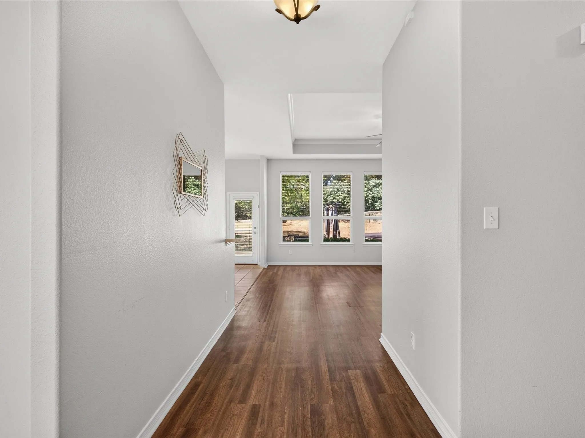 Wood-finish flooring throughout, recessed ceiling, multiple large windows, and a glass-paneled exterior door