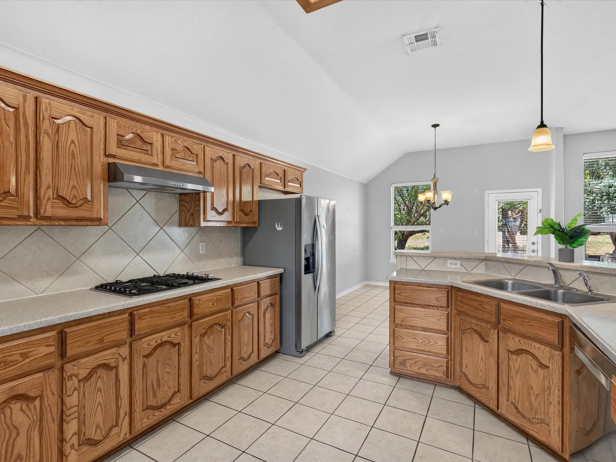 Wood-finish cabinetry, tile flooring, vaulted ceilings, dual basin sink, and stainless steel appliances