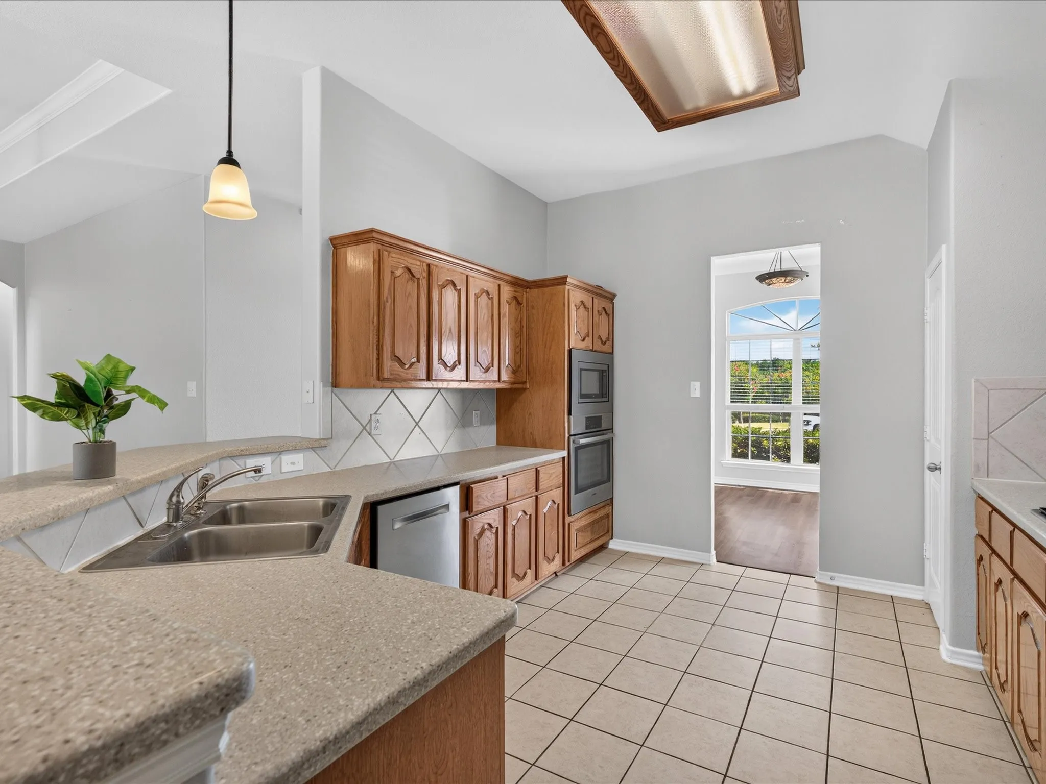 Kitchen featuring wood cabinetry, tiled flooring, integrated double wall ovens, a double basin sink, and a dishwasher