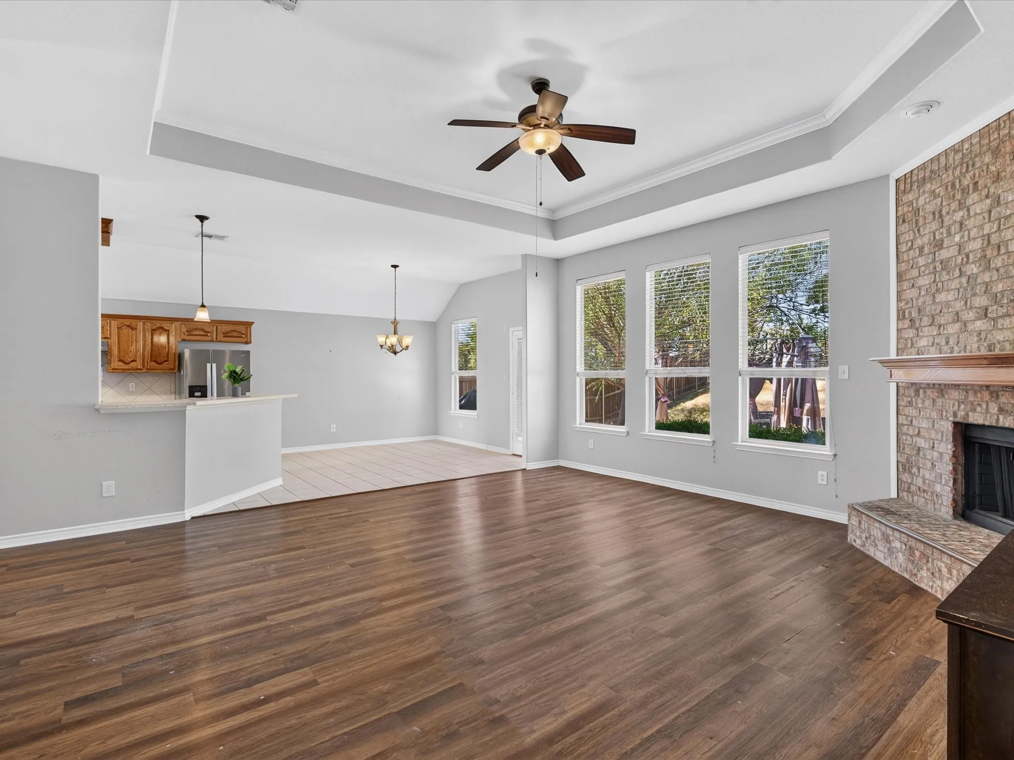 Spacious interior featuring wood-finish flooring, a tray ceiling with a ceiling fan, and a brick fireplace