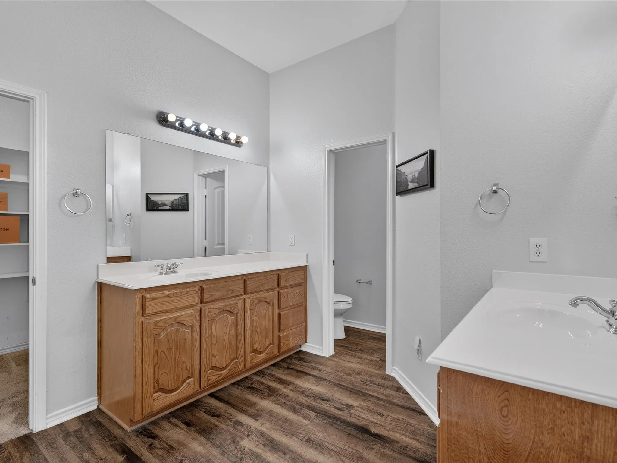 Wood-finish flooring, dual vanity setup with white countertops, and wood cabinetry