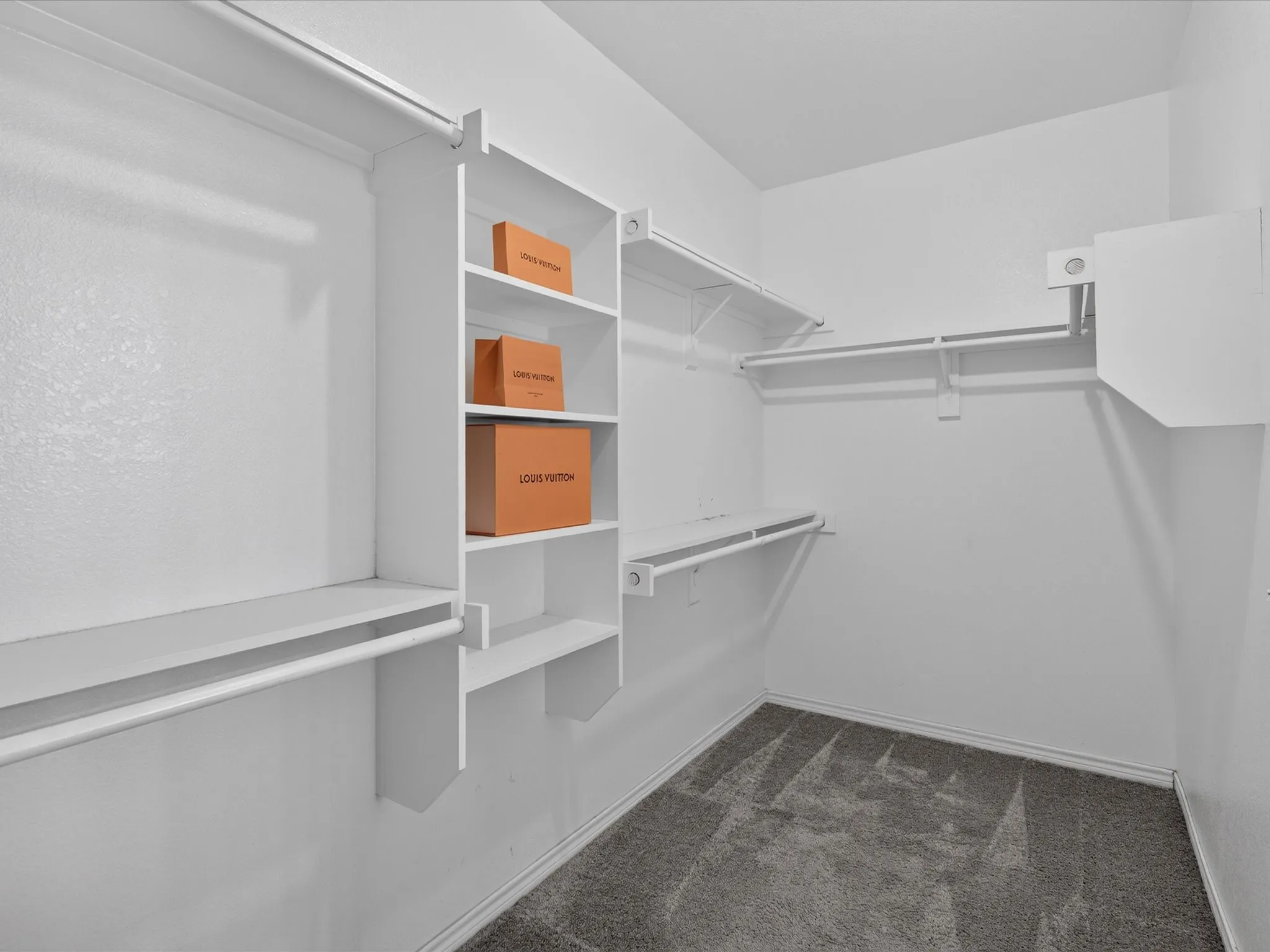 Walk-in closet featuring built-in shelving, multiple hanging rods, and dark gray carpeting