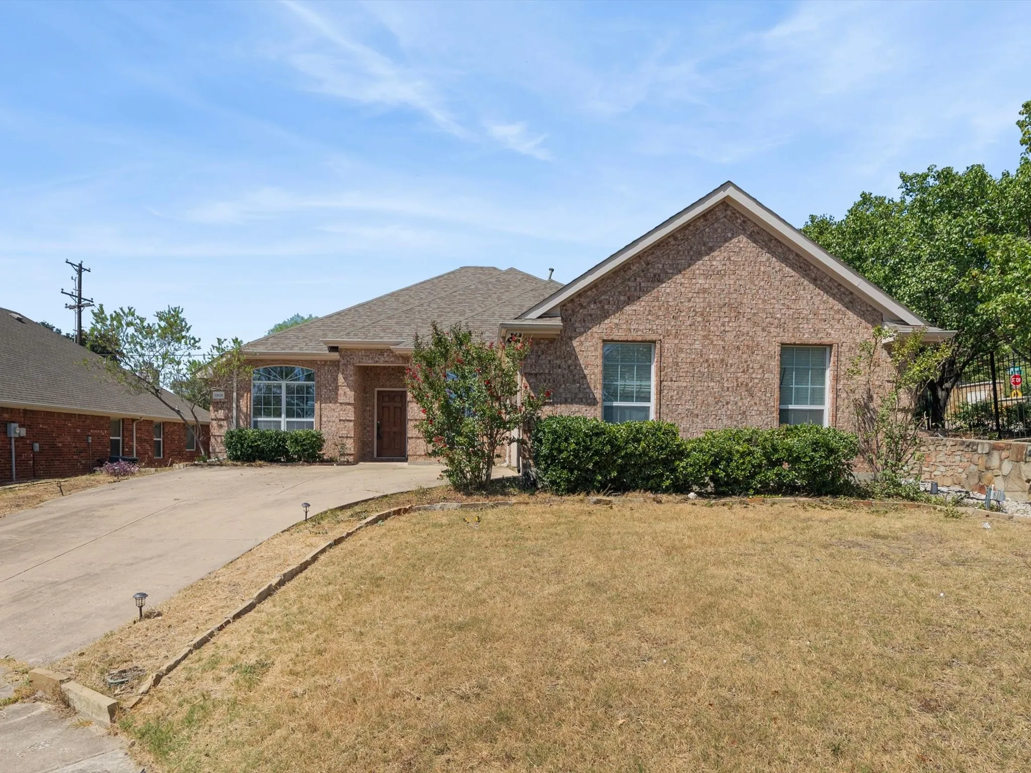 Brick exterior, arched window, attached garage, concrete driveway, and mature landscaping