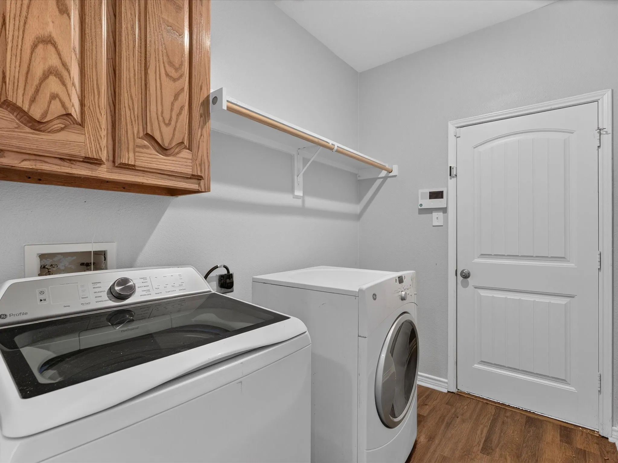 Laundry space featuring wood-finish flooring, overhead wood cabinetry, and a wall-mounted hanging rod