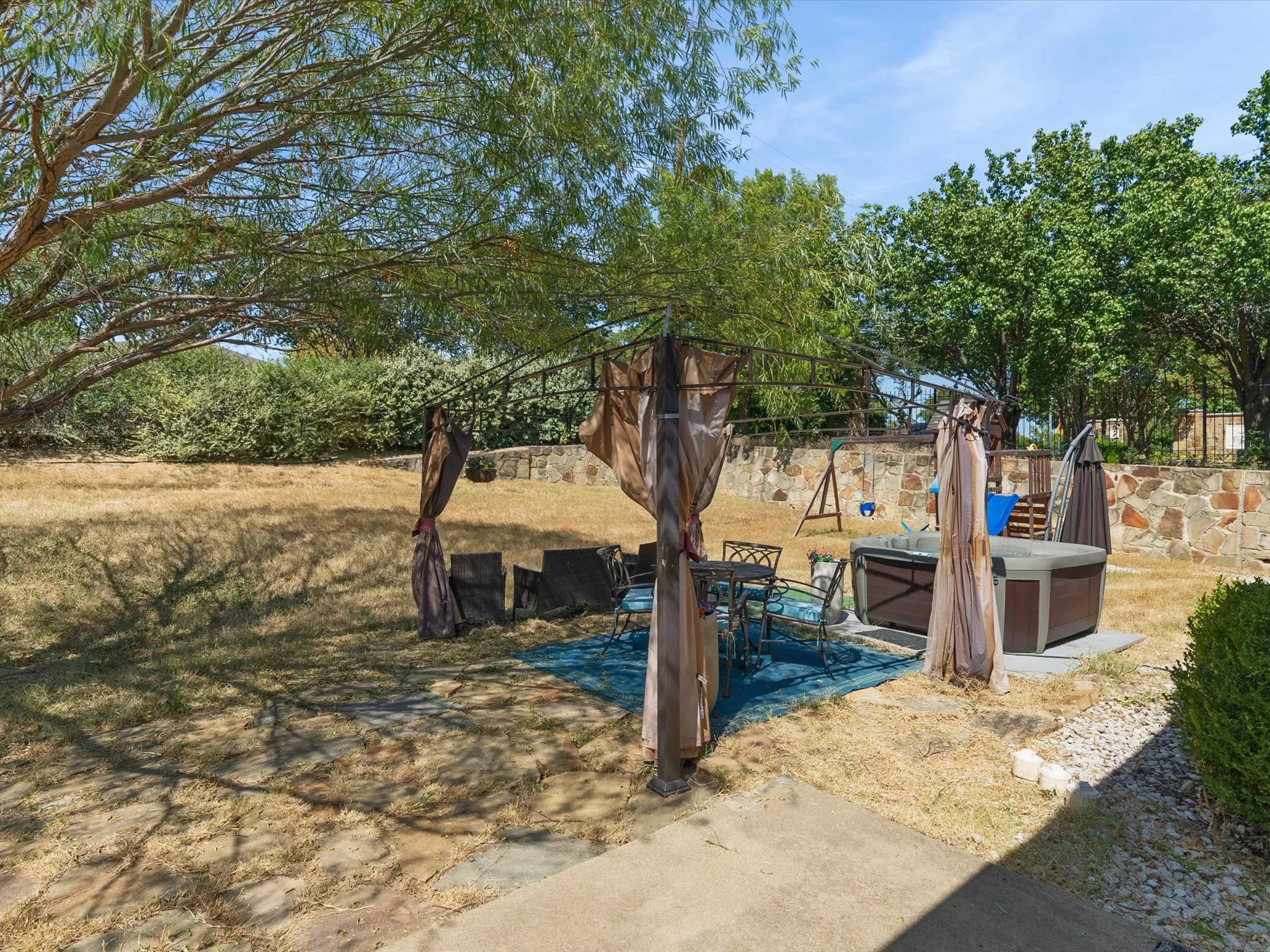 Backyard featuring a stone retaining wall, paved patio area, and a built-in spa