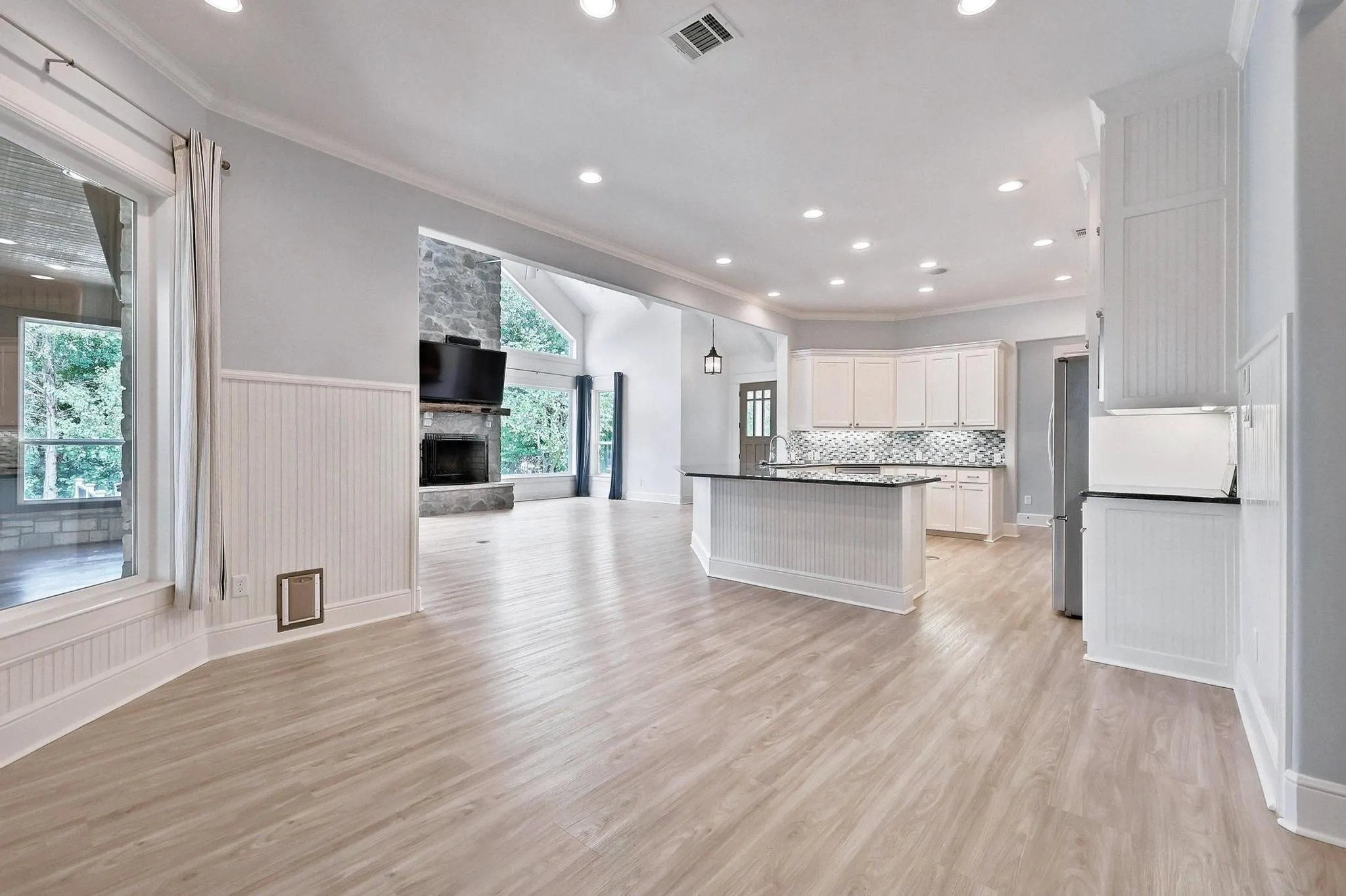 Wood-finish flooring throughout, beadboard wainscoting, recessed lighting, white cabinetry, and stainless steel appliances