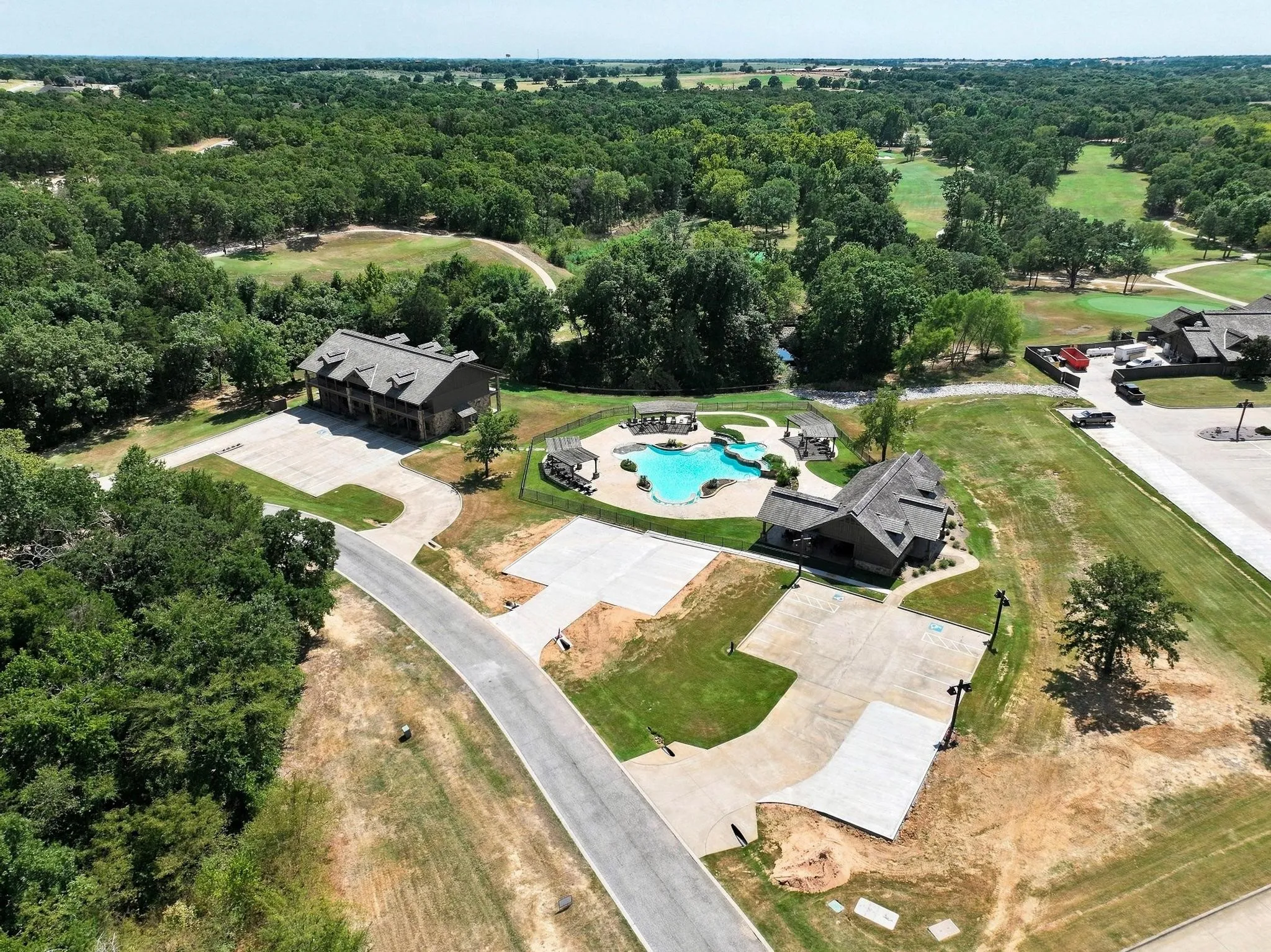 Swimming pool, adjacent buildings, paved parking areas, and surrounding treeline