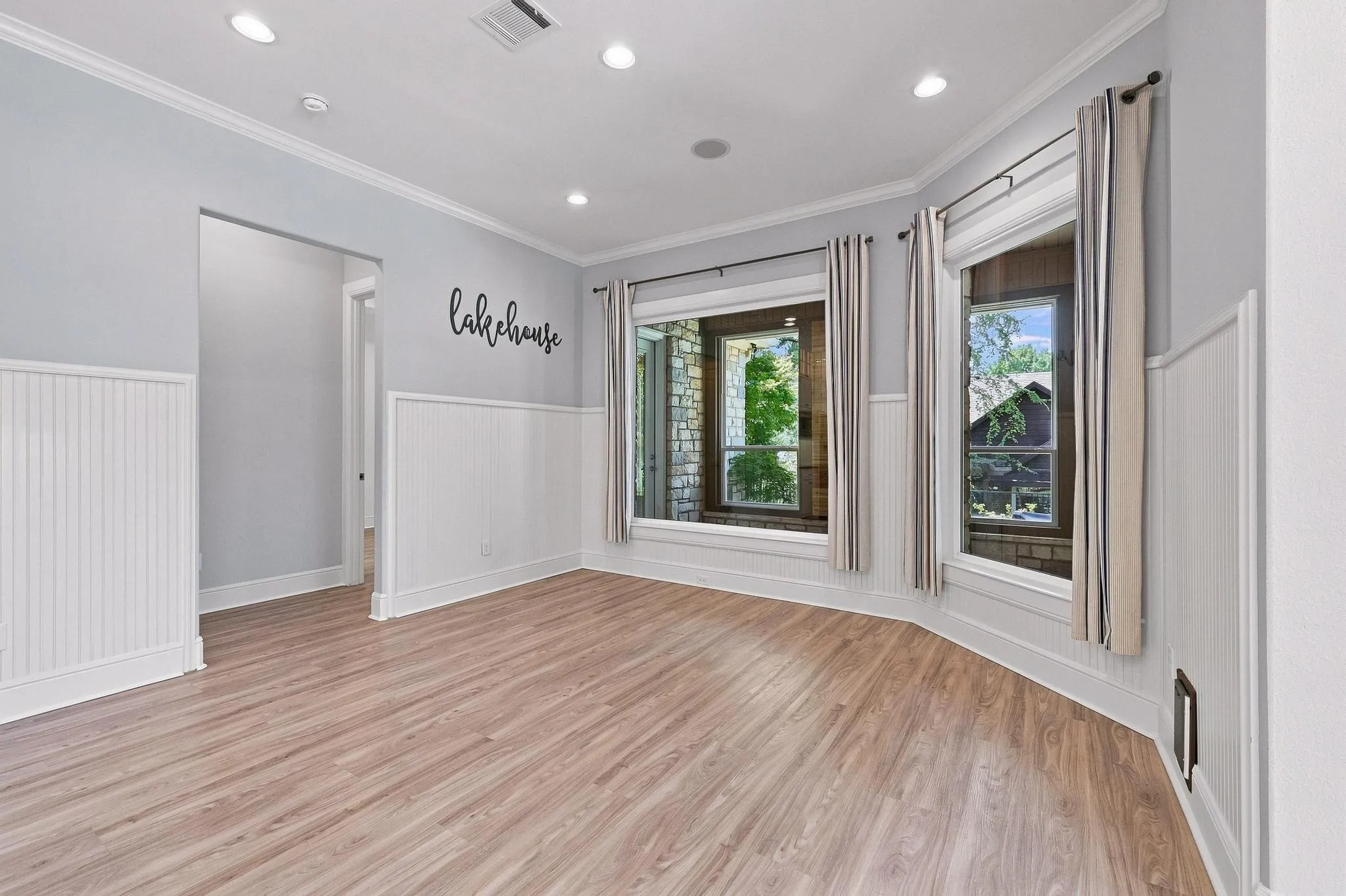 Light wood-finish flooring, white beadboard wainscoting, crown molding, recessed lighting, and multiple windows