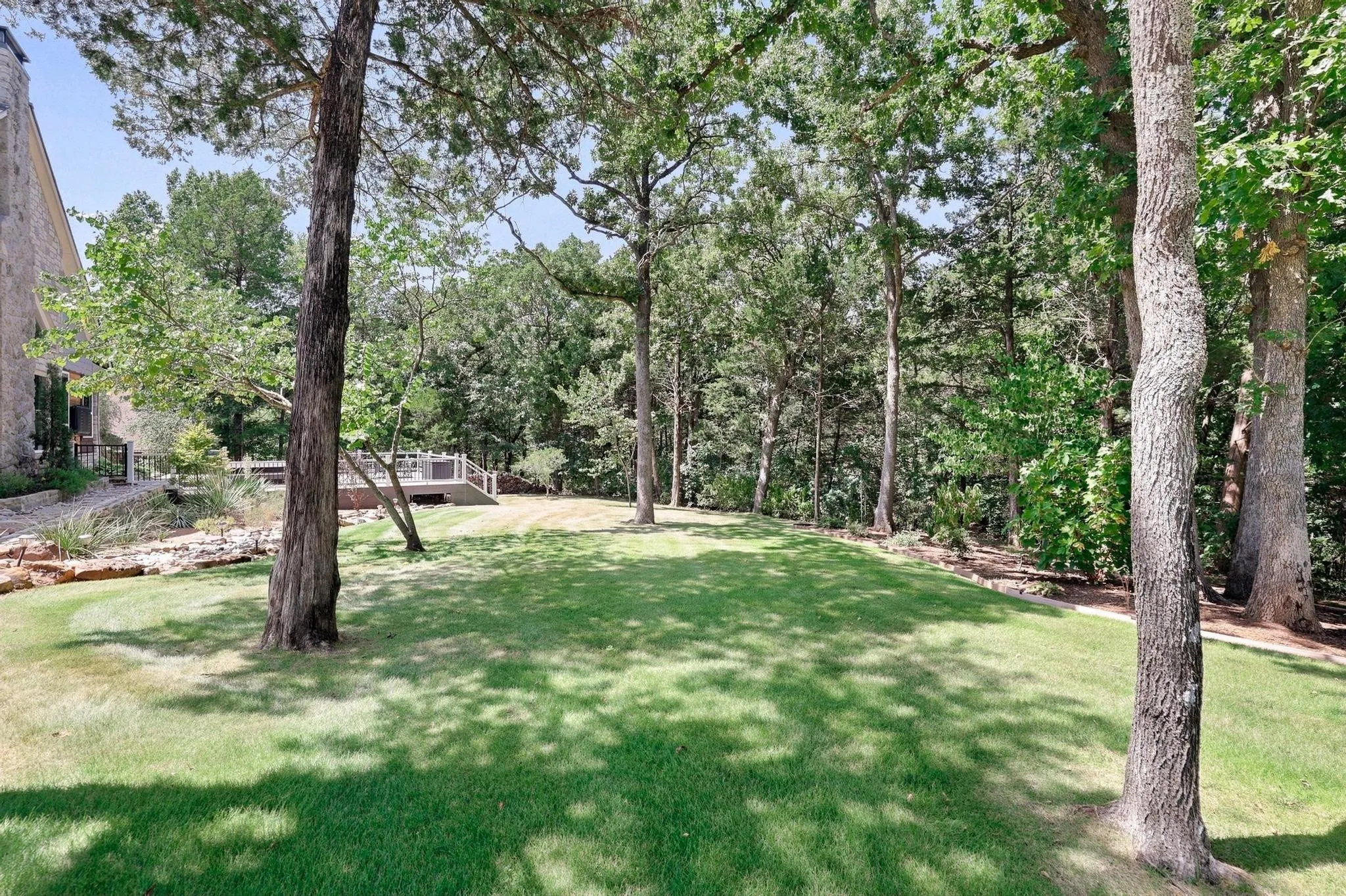 Expansive lawn featuring mature trees, a multi-level deck, and natural stone landscaping