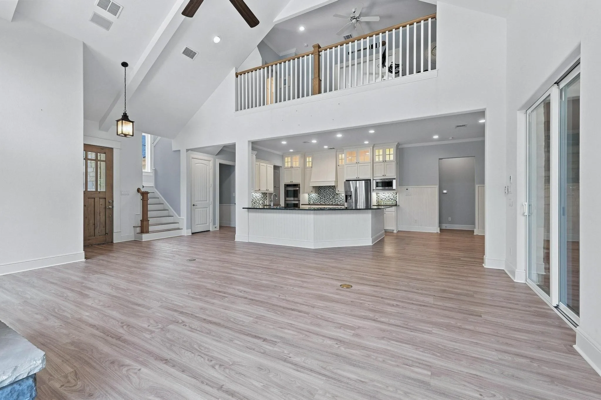 Vaulted ceilings with exposed beams, wood-finish flooring, a kitchen island with built-in appliances, stainless steel appliances, and a sliding glass door