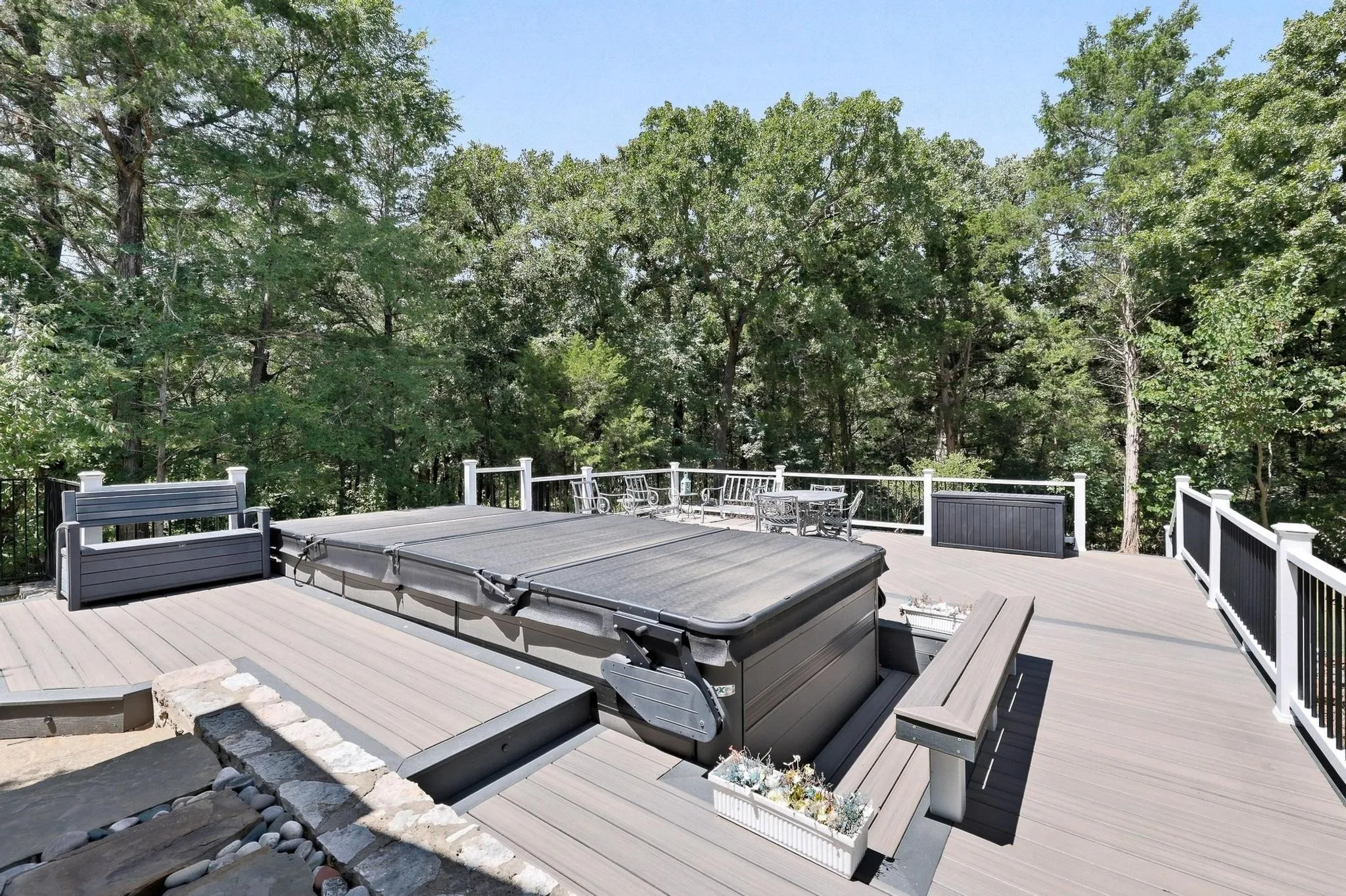 Expansive outdoor deck featuring a hot tub, composite decking, and white railings with black balusters