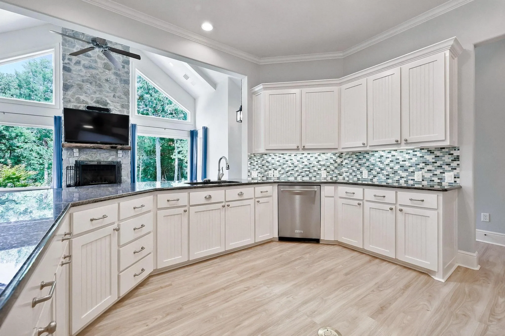 Contemporary kitchen featuring white cabinetry, dark countertops, a mosaic tile backsplash, stainless steel dishwasher, and wood-finish flooring