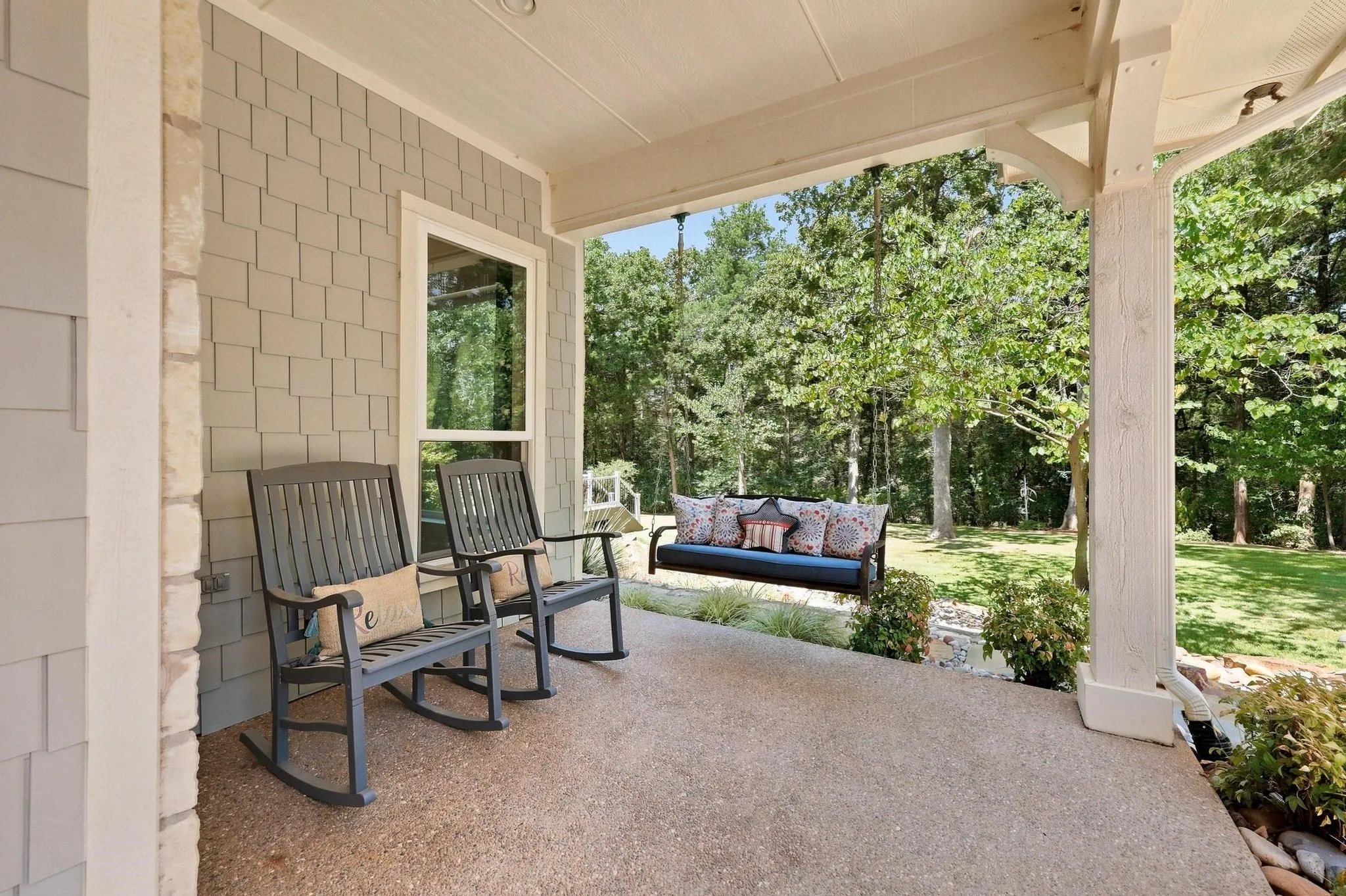 Covered porch with exposed aggregate concrete flooring, shaker siding, and stone accents