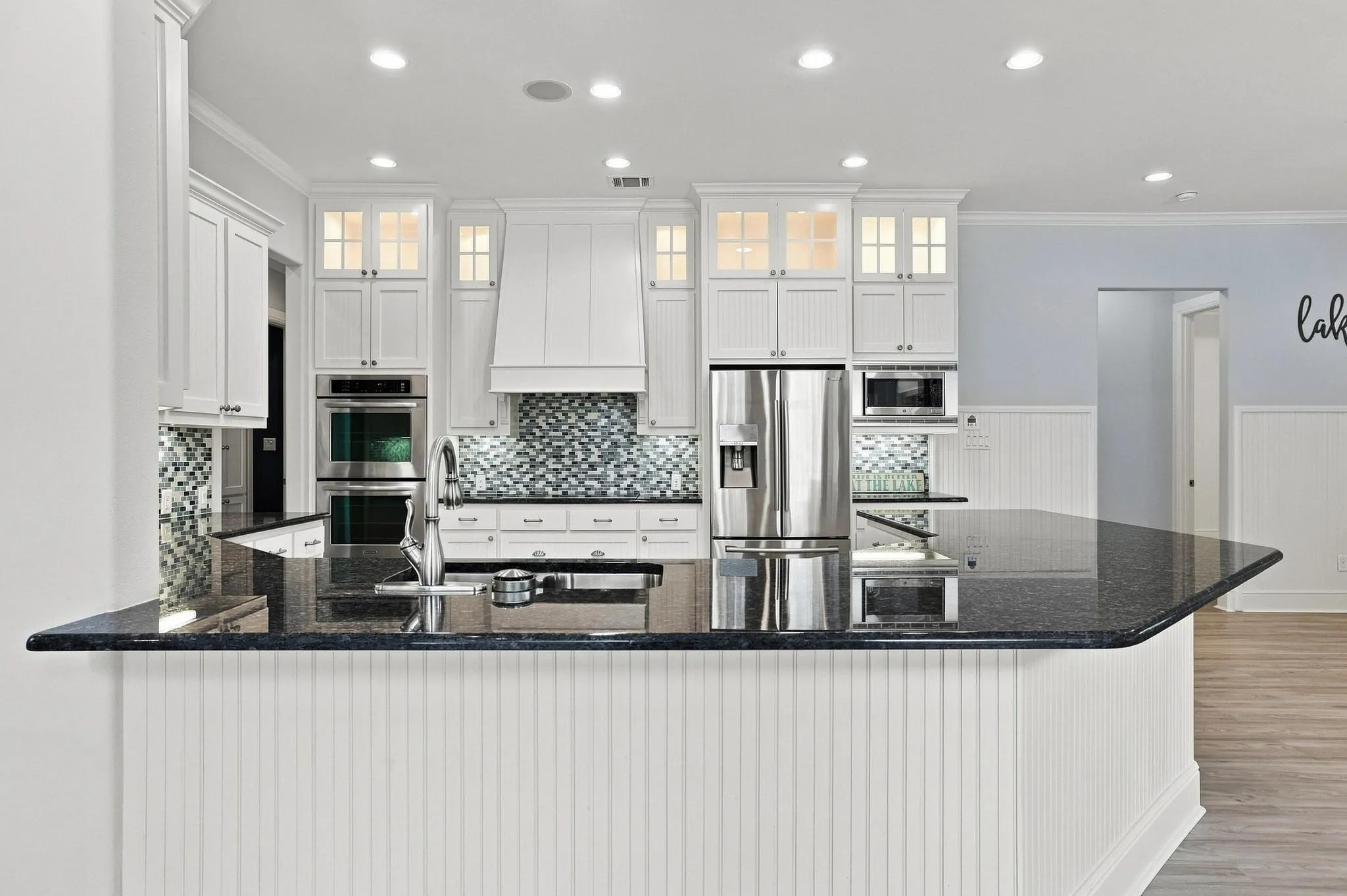 Kitchen featuring white shaker cabinetry, stainless steel appliances, dark stone countertops, mosaic tile backsplash, and a beadboard-paneled island