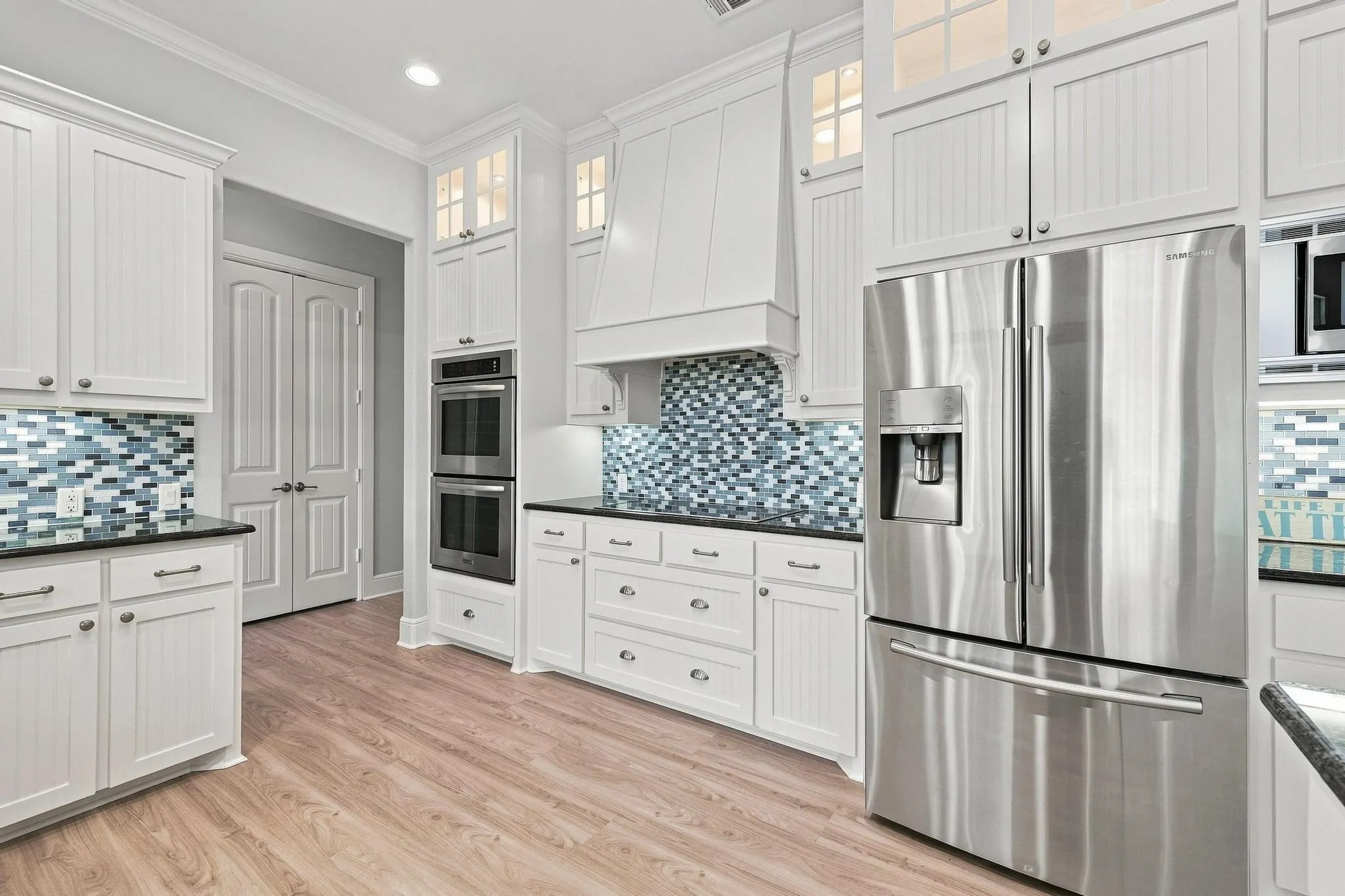 White cabinetry with beadboard paneling and glass-front upper cabinets, stainless steel appliances, dark countertops, and a mosaic tile backsplash
