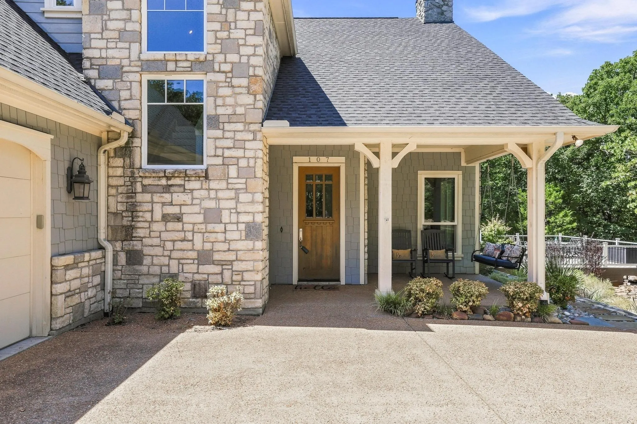 Stone and siding exterior with a covered porch, wood-paneled front door, and an attached garage