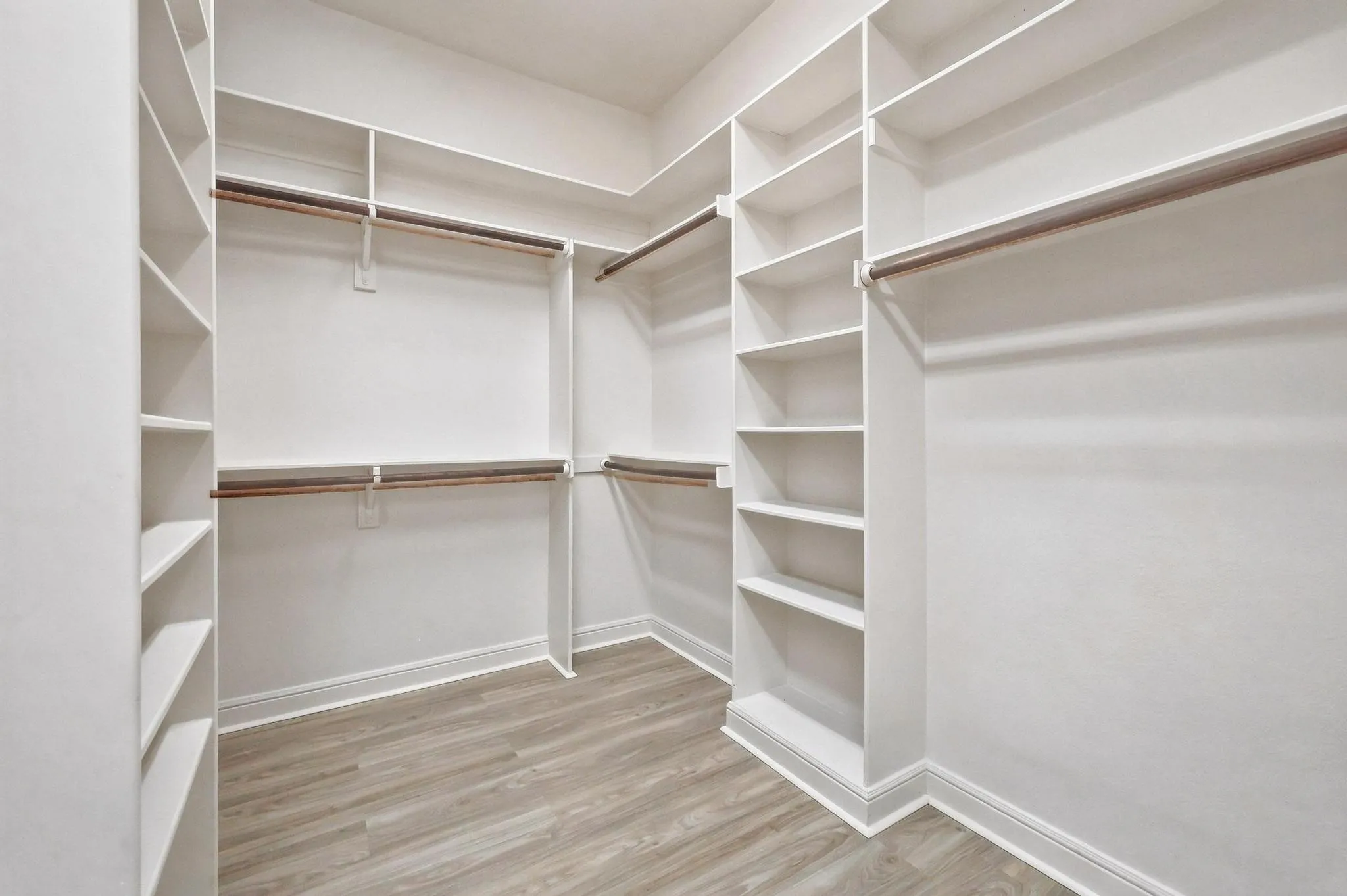 Primary suite Walk-in closet featuring built-in white shelving, multiple hanging rods, and wood-finish flooring
