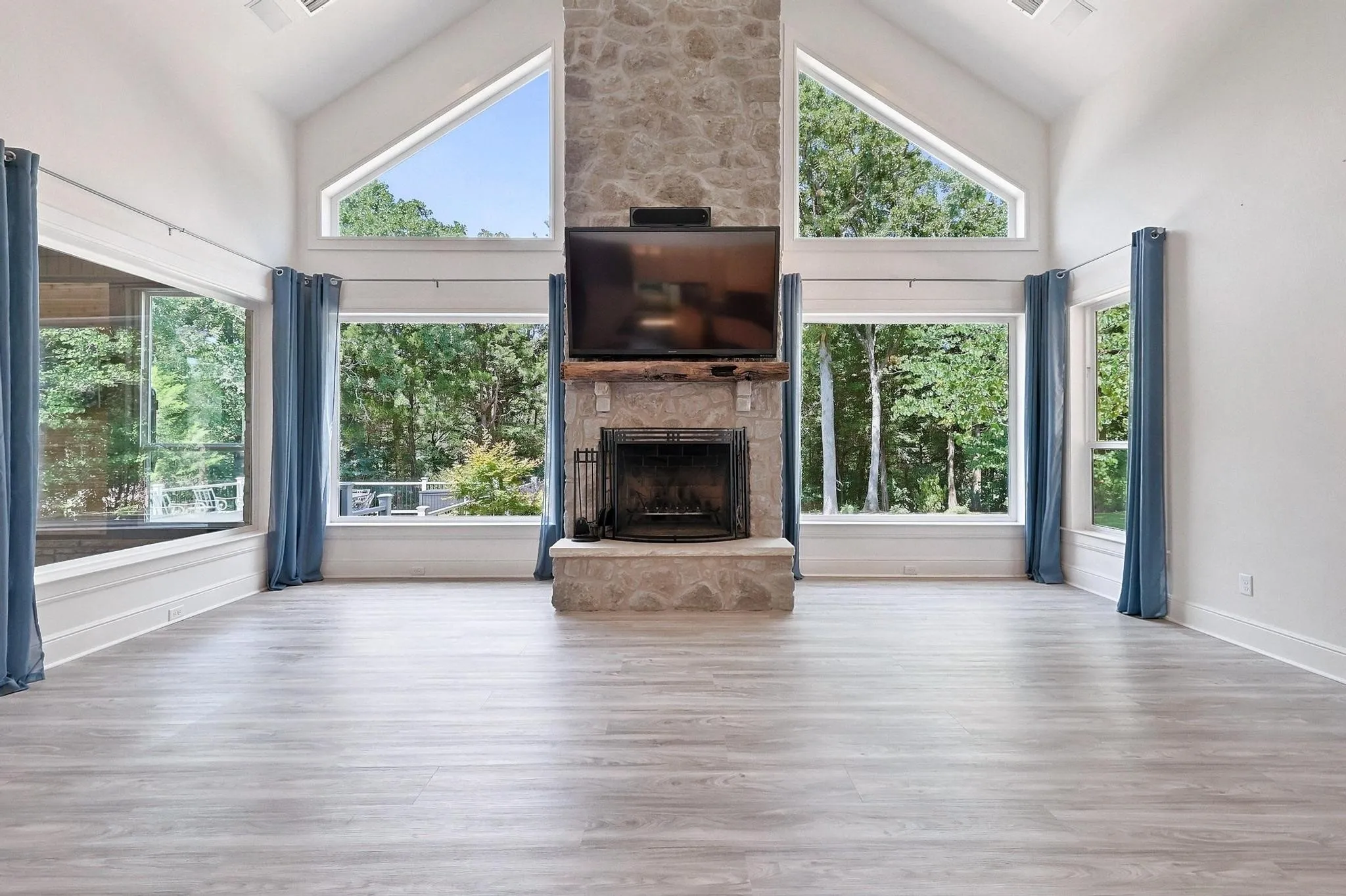 Stone fireplace with a wood mantle, vaulted ceiling with exposed beams, wood-finish flooring, and expansive windows