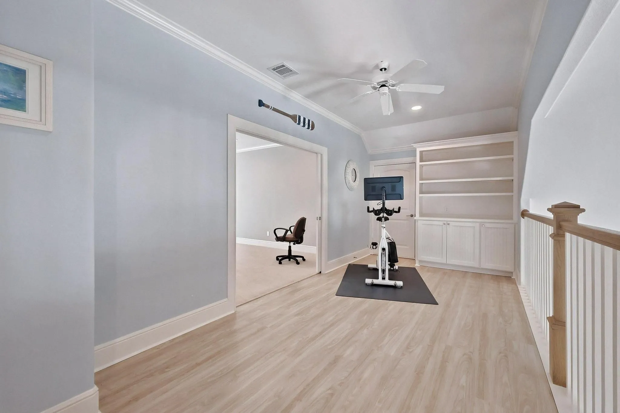 Wood-finish flooring with crown molding, built-in shelving, and a ceiling fan