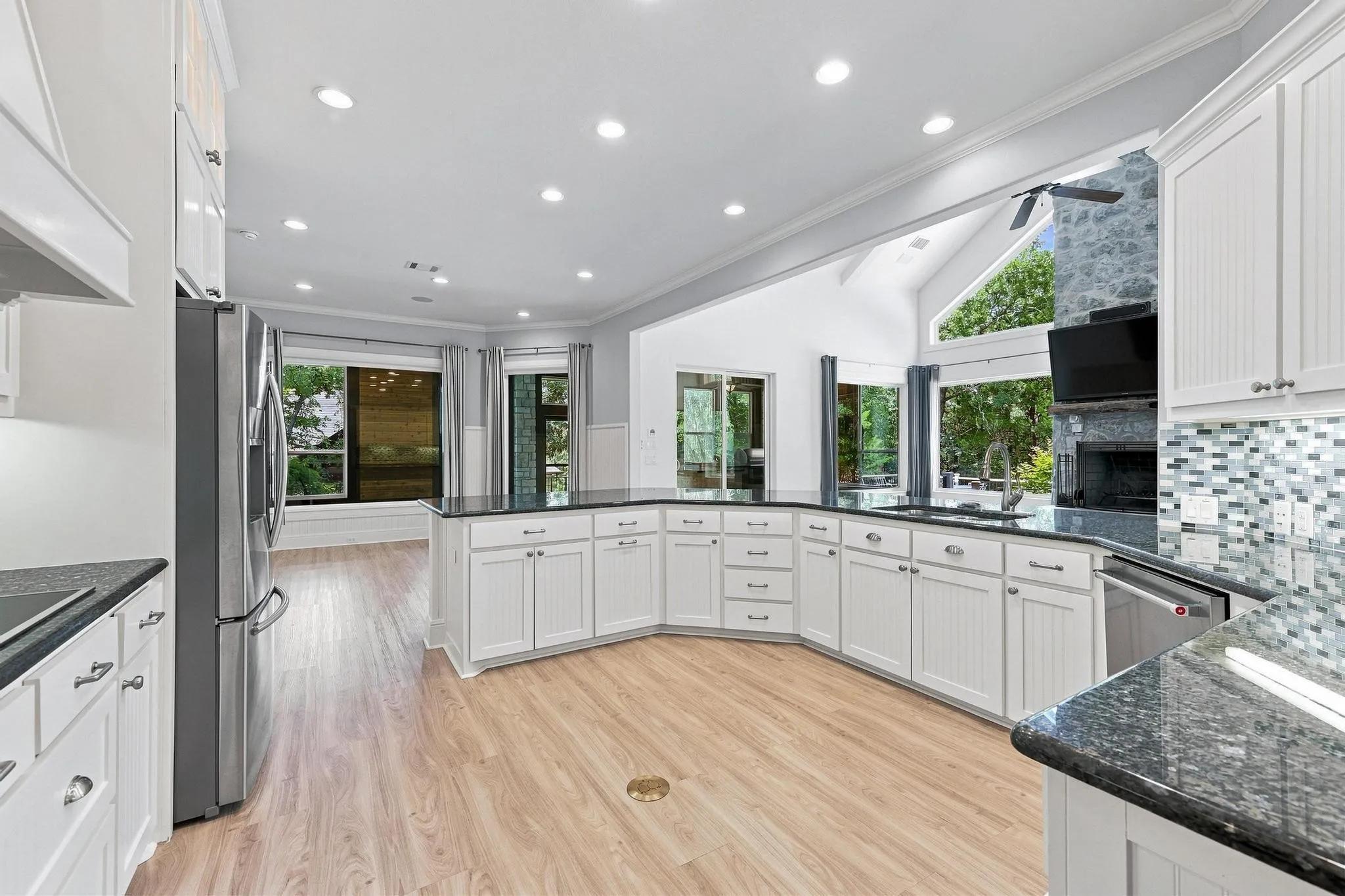 Spacious kitchen featuring white cabinetry, dark stone countertops, stainless steel appliances, wood-finish flooring, and a decorative tile backsplash